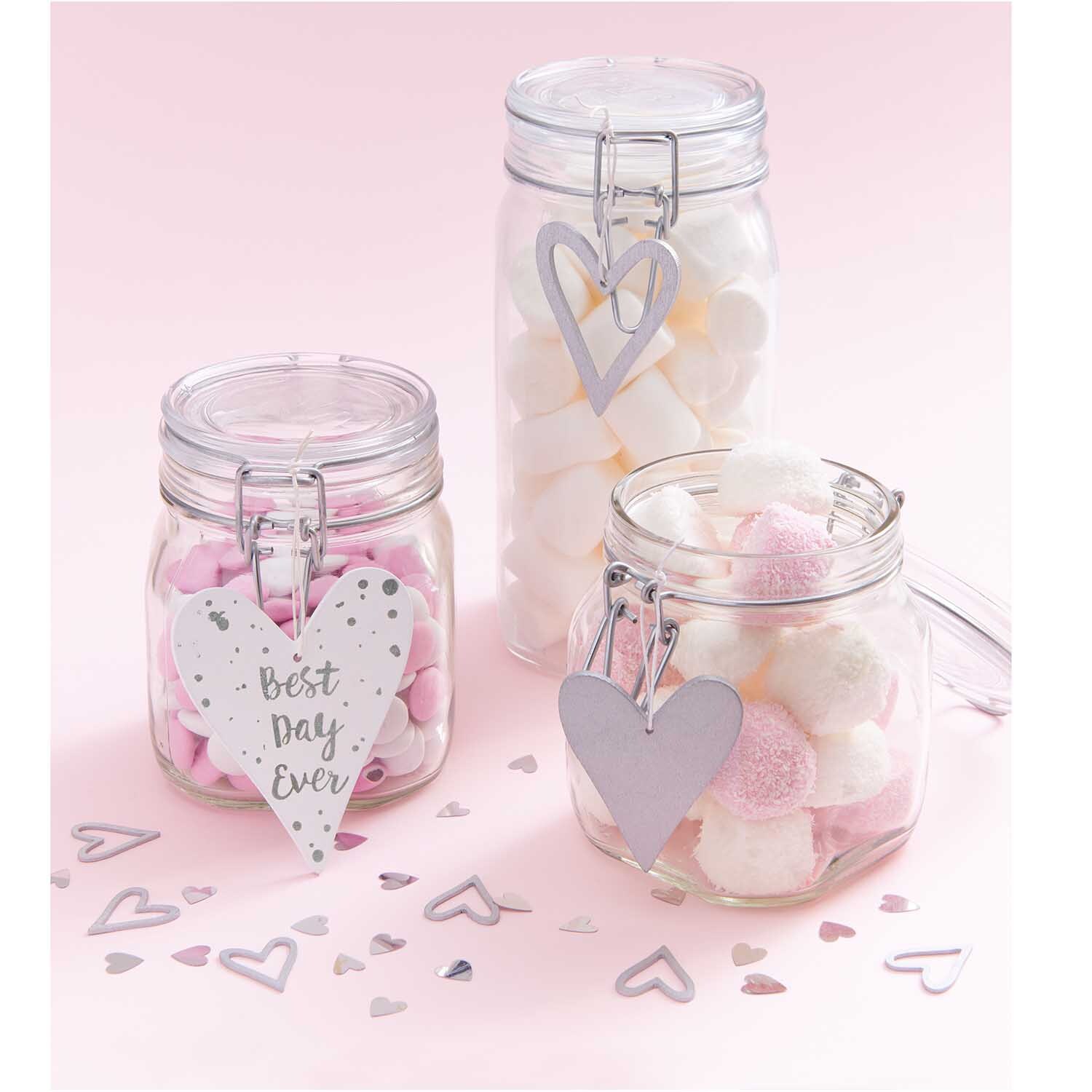 Holzhänger Herz silber von Rico Design Holzhänger Herz silber von Rico Design an Gläsern mit rosa und weißen Süßigkeiten auf rosa Hintergrund.