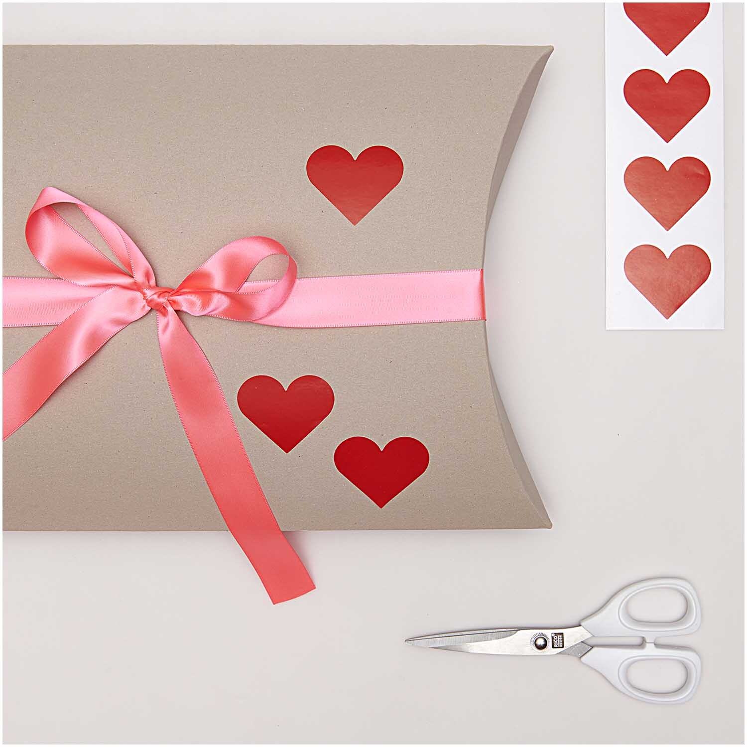 Paper Poetry Sticker Herzen 5cm 120 Stück auf der Rolle Farbe Rot von Rico Design Paper Poetry Sticker Herzen 5cm 120 Stück auf der Rolle. Geschenkverpackung mit roten Herzstickern und rosa Schleife, daneben eine Schere.