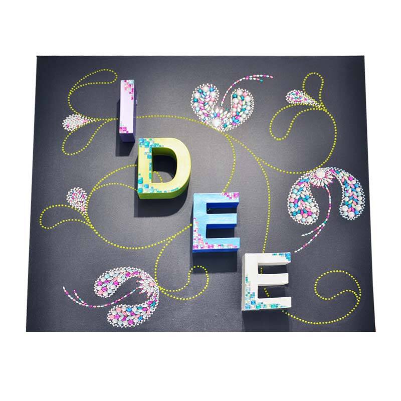 Pappbuchstabe & von Rico Design 3D Papp-Buchstaben stehend auf schwarzem Hintergrund, dekoriert mit floralen Mustern und gelben Linien.