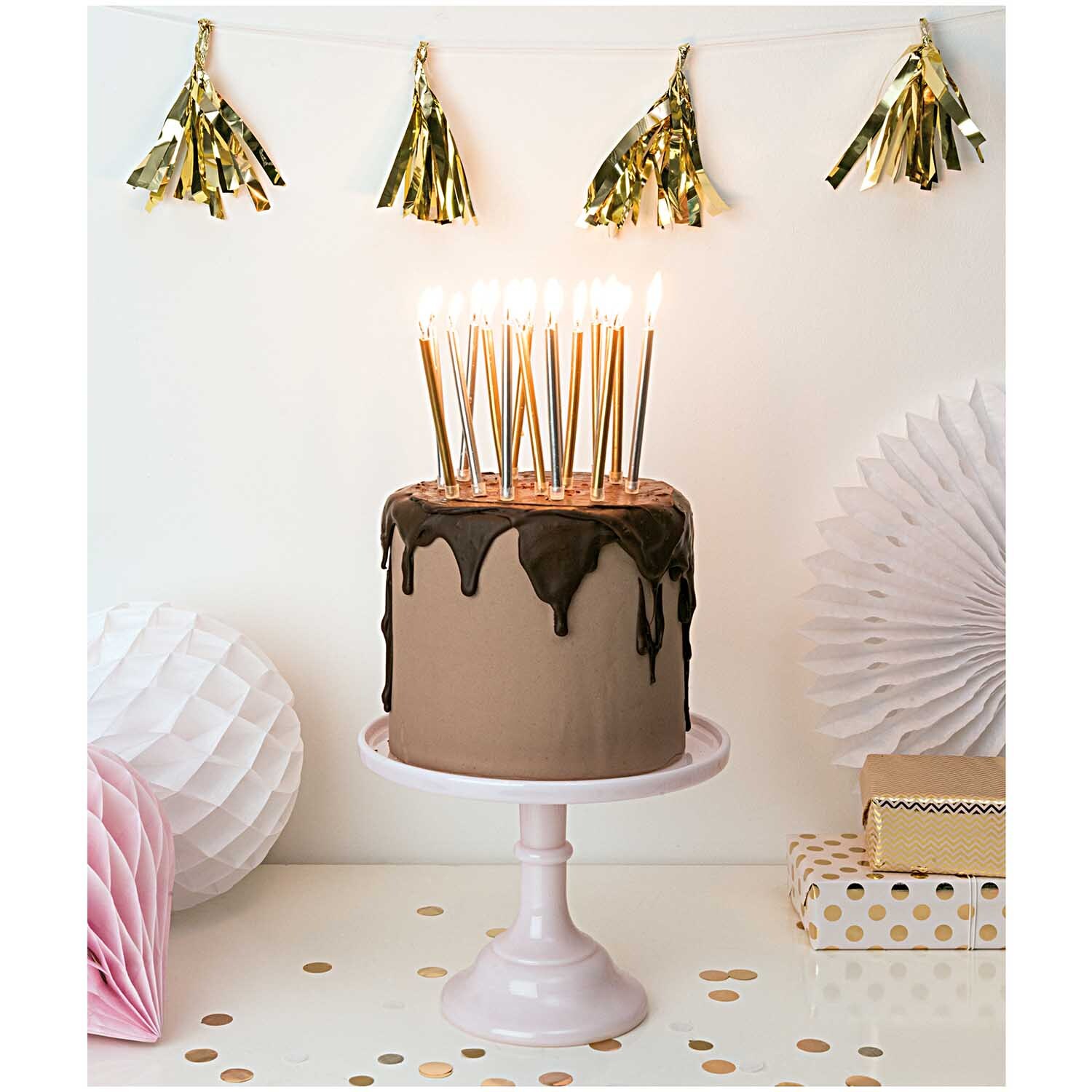Paper Poetry Girlande Quasten gold 2,8m von Rico Design Paper Poetry Girlande Quasten in Gold schmücken eine festliche Torte mit Kerzen auf einem Tisch.