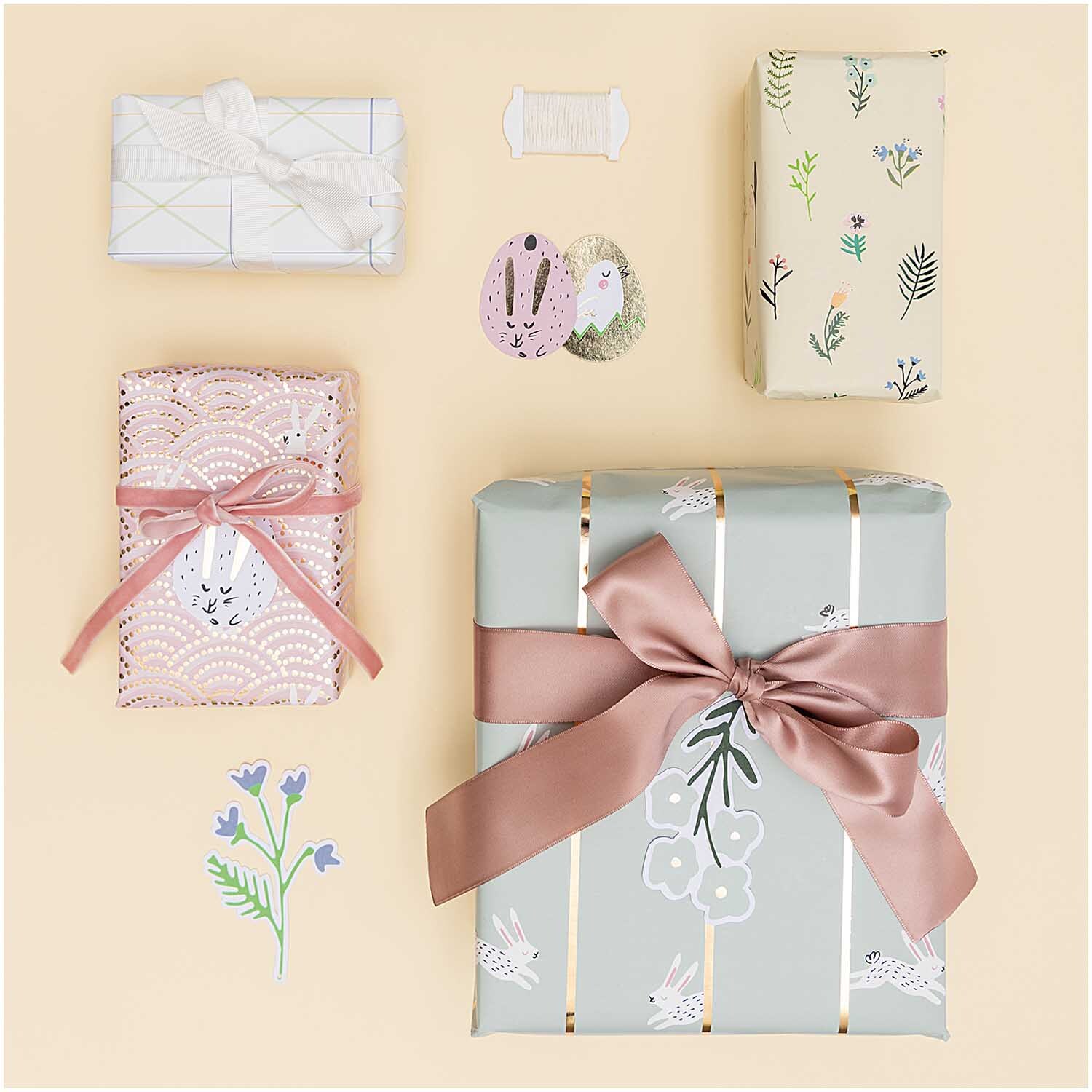 Paper Poetry Geschenkpapier Bunny Hop Hasen im Feld rosa 70cm 2m Hot Foil von Rico Design Paper Poetry Geschenkpapier Bunny Hop: Vier Geschenke in pastellfarbenem Papier mit floralen Mustern und rosa Schleifen dekoriert.