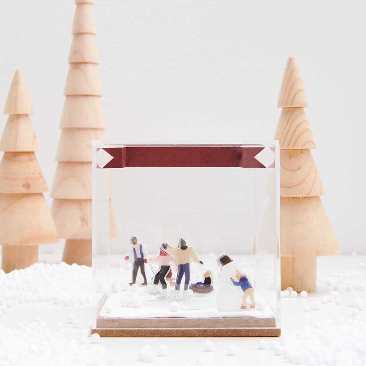 Figurico Gelsticker Schneevergnügen von Rico Design Figurico Gelsticker Schneevergnügen zeigt eine winterliche Szene mit Figuren in einem klaren Würfel, umgeben von Holz-Tannenbäumen.