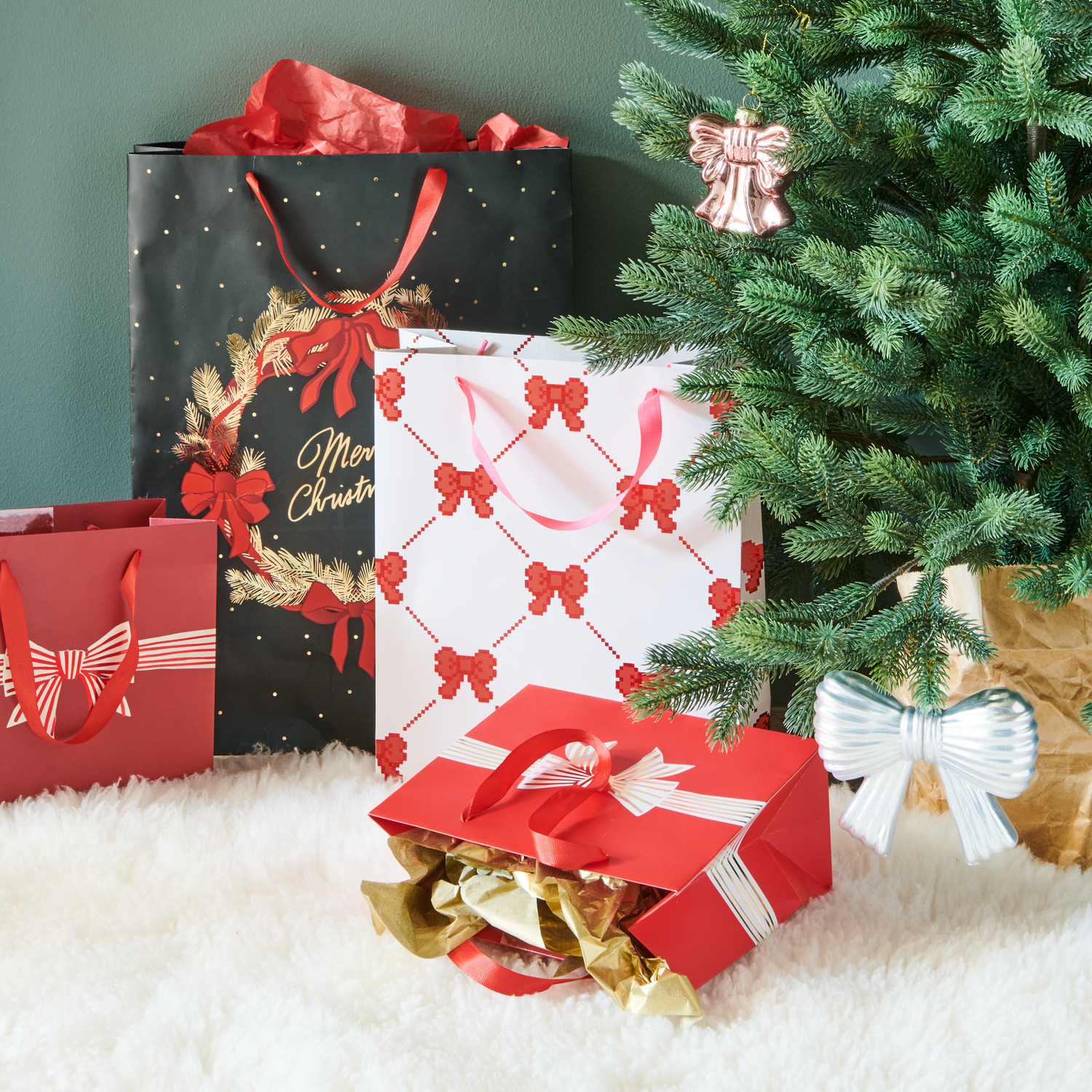 Geschenktüte Pixel Schleifen Creme L 26x32x12cm, 230g/m² von Rico Design Geschenktüte Pixel Schleifen Creme L von Rico Design unter einem Weihnachtsbaum, umgeben von weiteren festlichen Geschenktüten.