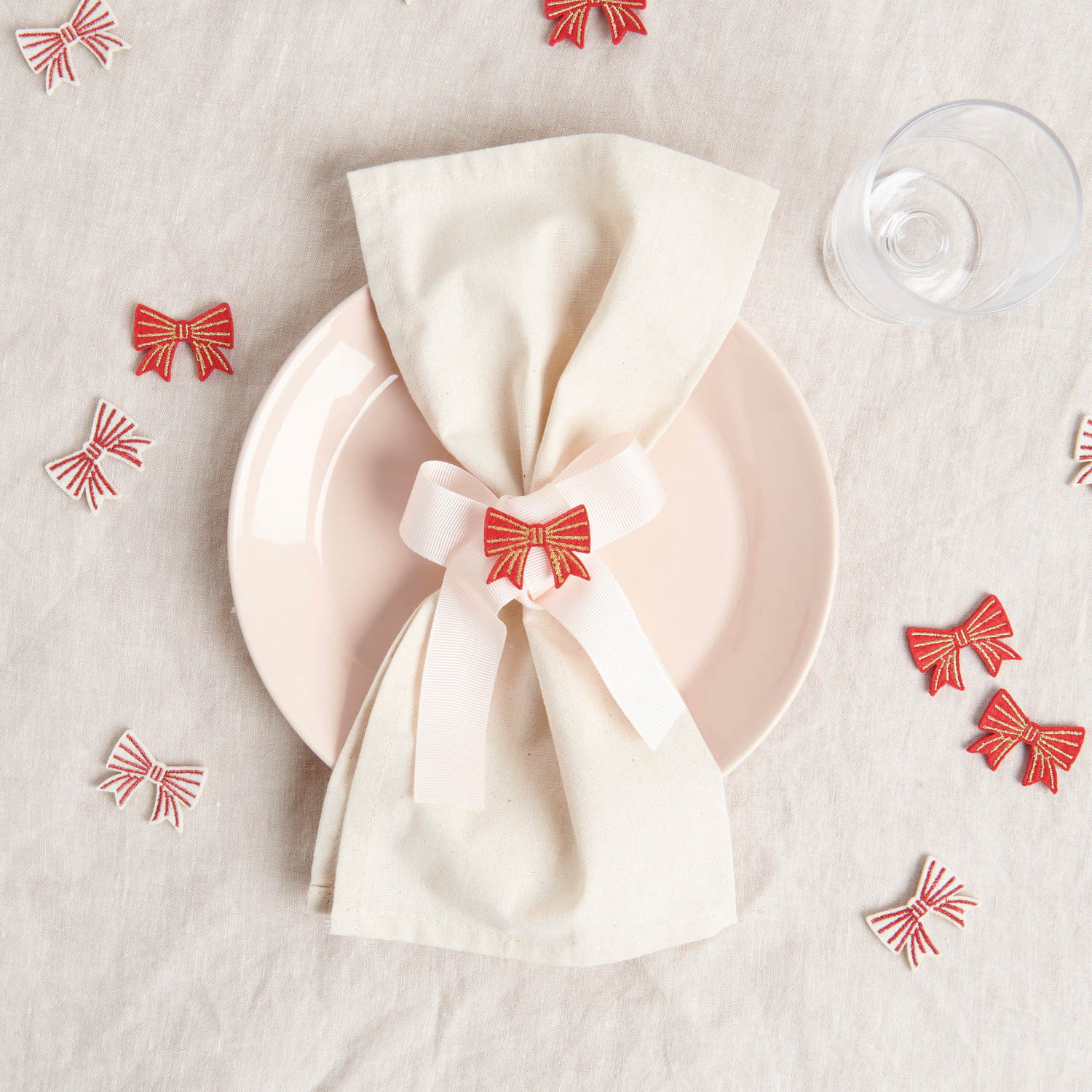 Filzstreu Schleifen 8 Stück Farbe Rot-Gold von Rico Design Filzstreu Schleifen dekorieren einen Tisch mit weißem Tuch, rosa Teller und Glas. Rot-goldene Schleifen von Rico Design, 8 Stück.