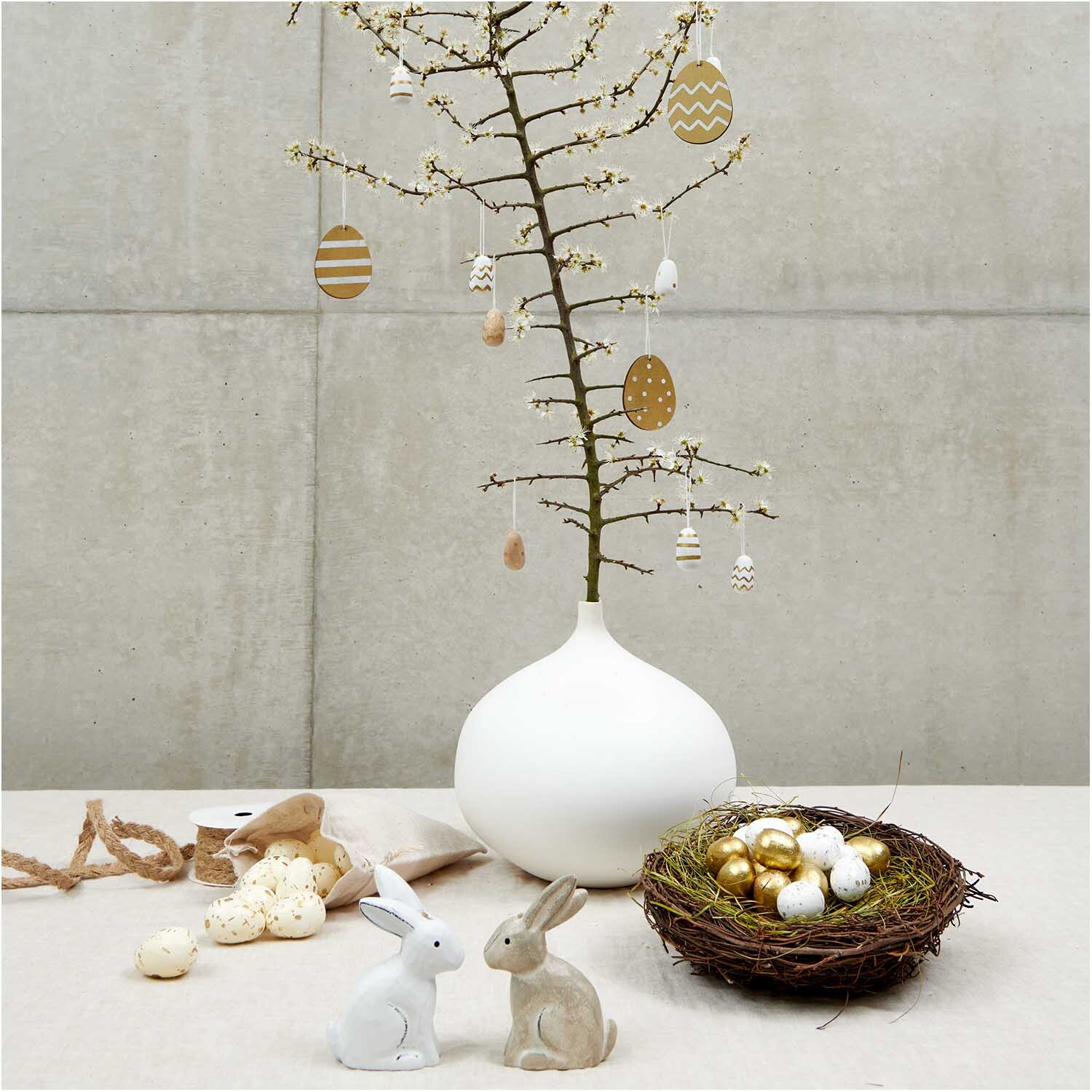 Eier im Netz 4cm 24 Stück von Rico Design Eier im Netz 4cm 24 Stück: Dekorative Ostereier an einem minimalistischen Baum in einer weißen Vase, umgeben von Hasenfiguren und einem Nest.