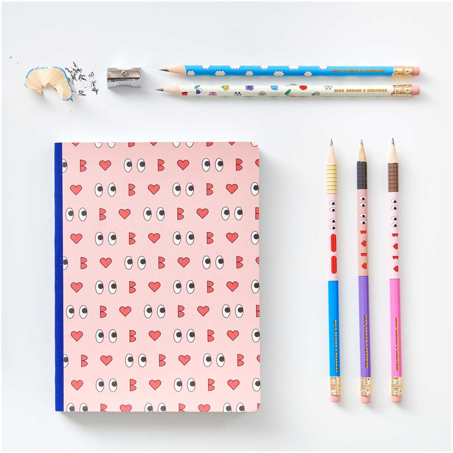 Rico Design x Redfries Bleistifte Eye Candy 5er-Set von Rico Design Rico Design x Redfries Bleistifte Eye Candy 5er-Set neben einem Notizbuch mit Augen- und Herzmotiven, umgeben von einem Anspitzer und Radiergummi.