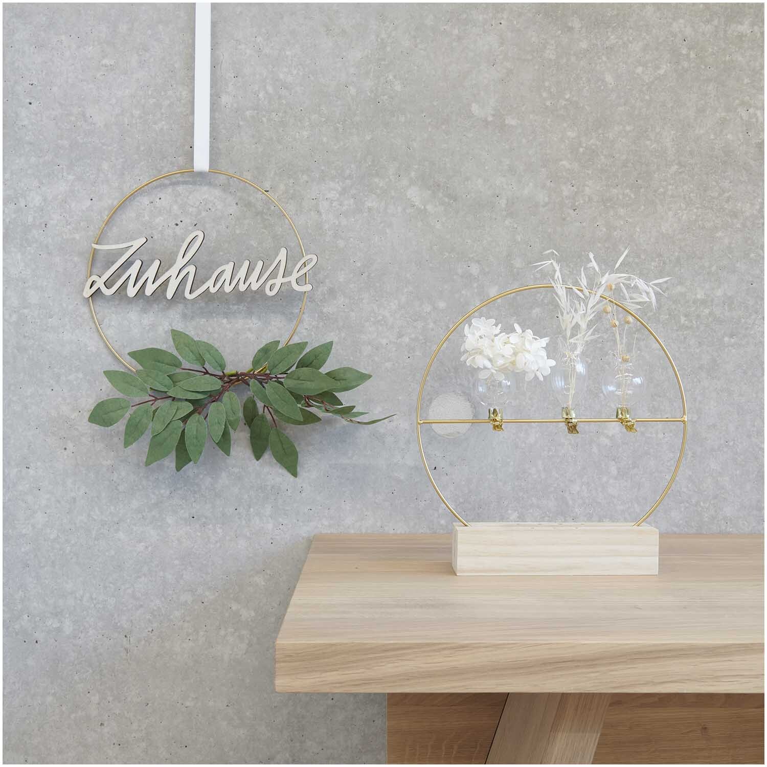Metallring mit Querstrebe Ø25cm, dekoriert mit grünen Blättern und weißen Blumen auf Holz.