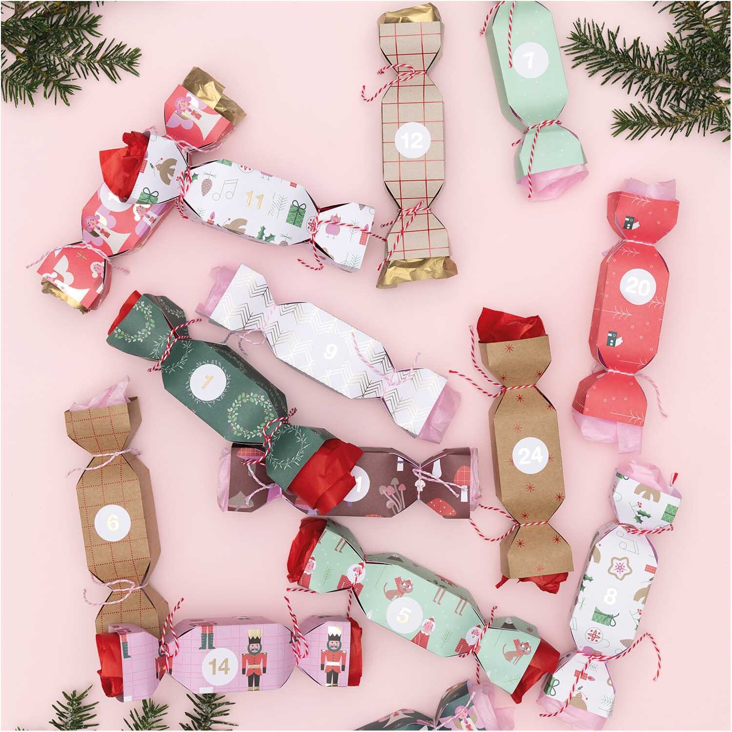 Paper Poetry Adventskalender Sticker Zahlen 1-24 auf bunten, weihnachtlich verpackten Bonbons, dekoriert mit Tannenzweigen.