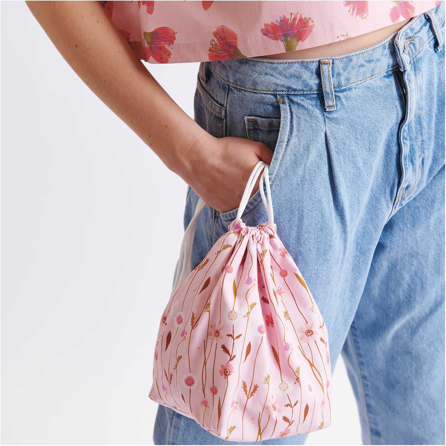 Meterware Druckstoff Wildblumen rosa von Rico Design Meterware Druckstoff Wildblumen rosa: Frau in Jeans hält rosa Beutel mit Wildblumenmuster von Rico Design.