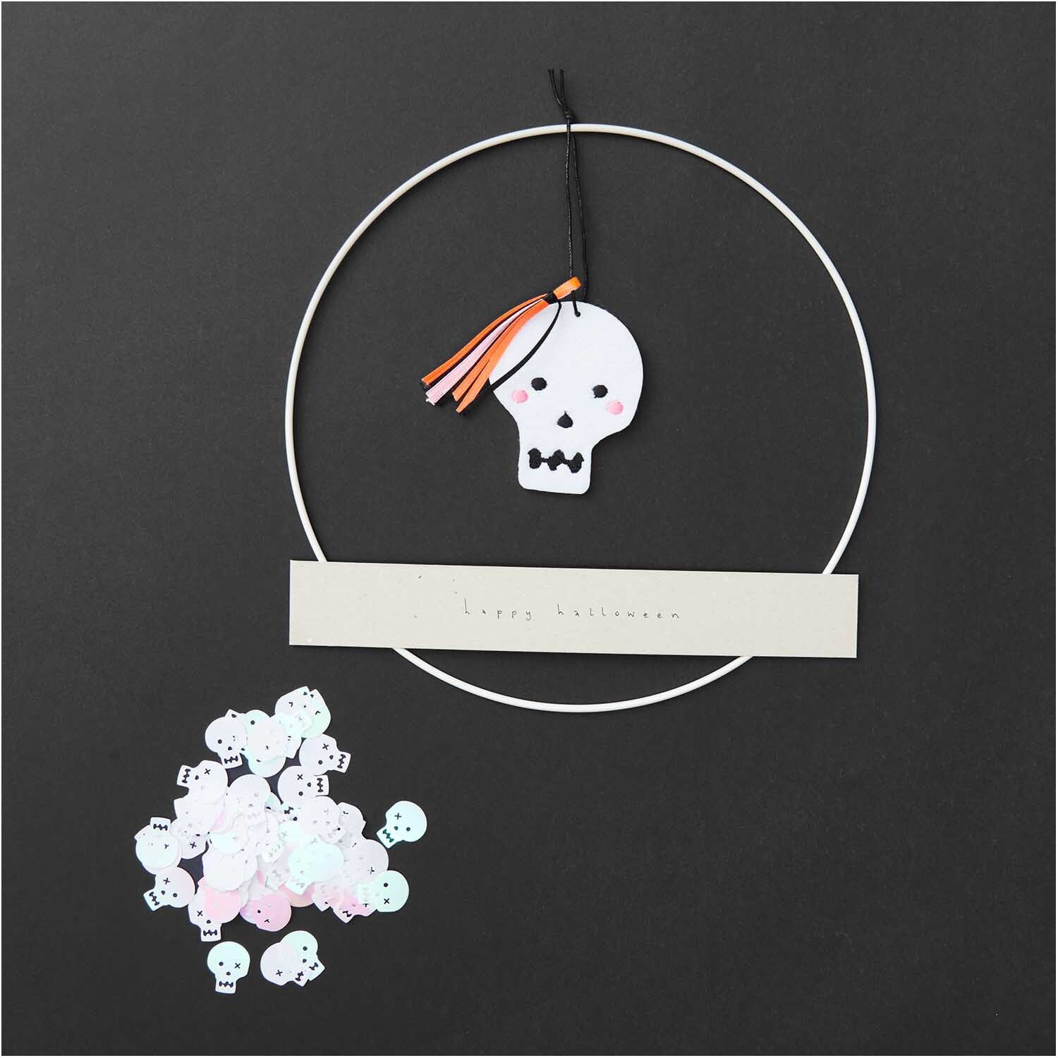 Filzhänger Totenkopf weiß 8x6,5cm von Rico Design Filzhänger Totenkopf weiß 8x6,5cm von Rico Design: Ein weißer Totenkopf-Anhänger mit bunten Bändern auf schwarzem Hintergrund.