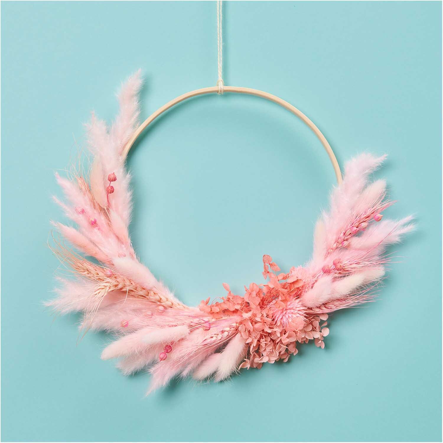 Getrockneter Lagurus pink ca. 40cm 50 Stück von Rico Design Getrockneter Lagurus pink ca. 40cm 50 Stück von Rico Design: Ein dekorativer Kranz aus rosa Trockenblumen auf hellblauem Hintergrund.