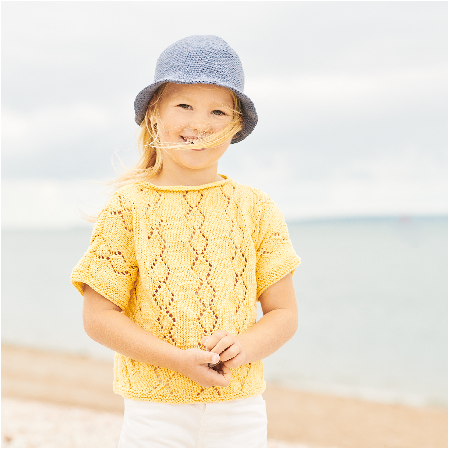 Essentials Organic Cotton dk 50g 105m Couleur Moutarde from Rico Design Essentials Organic Cotton dk: Kind am Strand in gestricktem, senffarbenem Oberteil und blauem Hut. Ideal für sommerliche Tage.