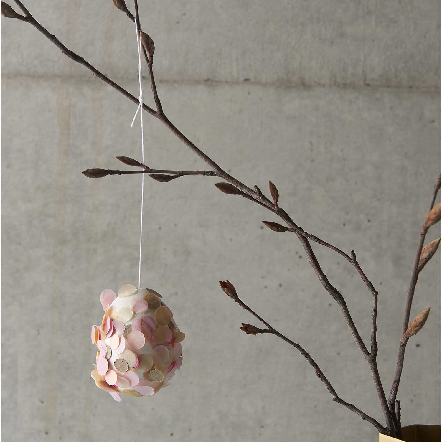Konfetti rosa 20g von Rico Design Konfetti rosa 20g: Ein dekorativer Zweig mit einem hängenden Ei, verziert mit rosa Konfetti von Rico Design.