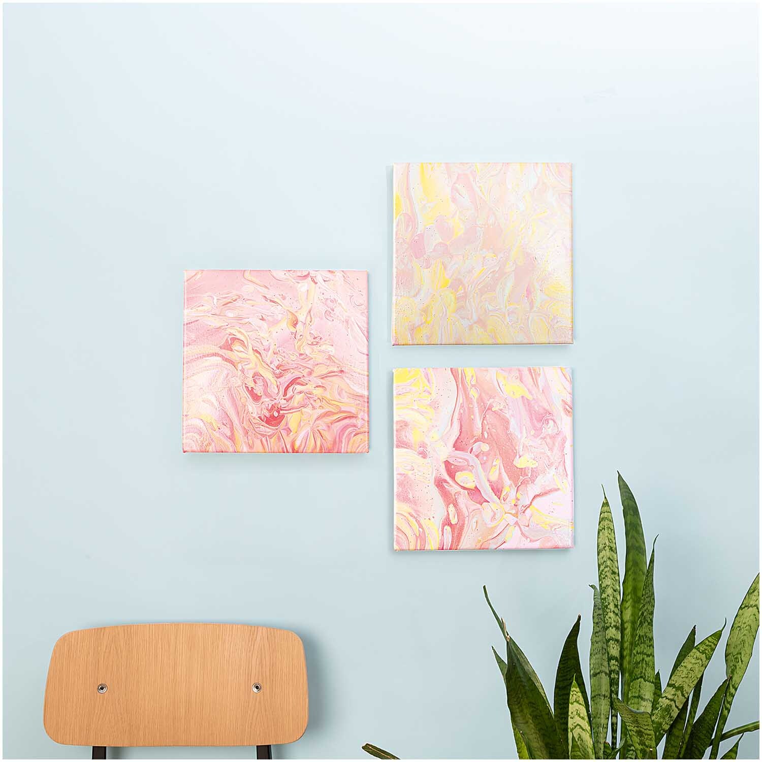 Super Canvas Keilrahmen 3er Set 20x20cm von Rico Design Super Canvas Keilrahmen 3er Set von Rico Design, bemalt mit abstrakten rosa und gelben Mustern, an einer hellblauen Wand über einem Stuhl und Pflanzen.