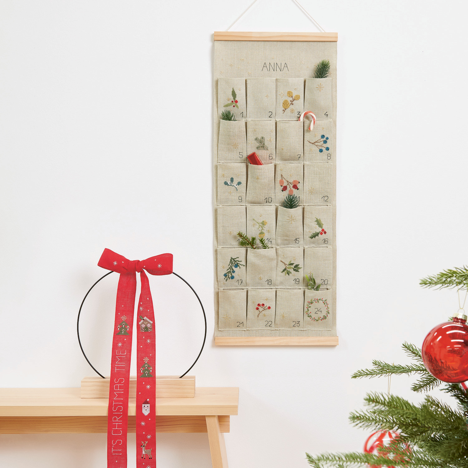 Stickpackung Schleife It's Christmas Time 22x58cm von Rico Design Stickbuch Put a Bow on It Nr. 185: Adventskalender mit Taschen und roter Schleife, dekoriert mit weihnachtlichen Motiven.