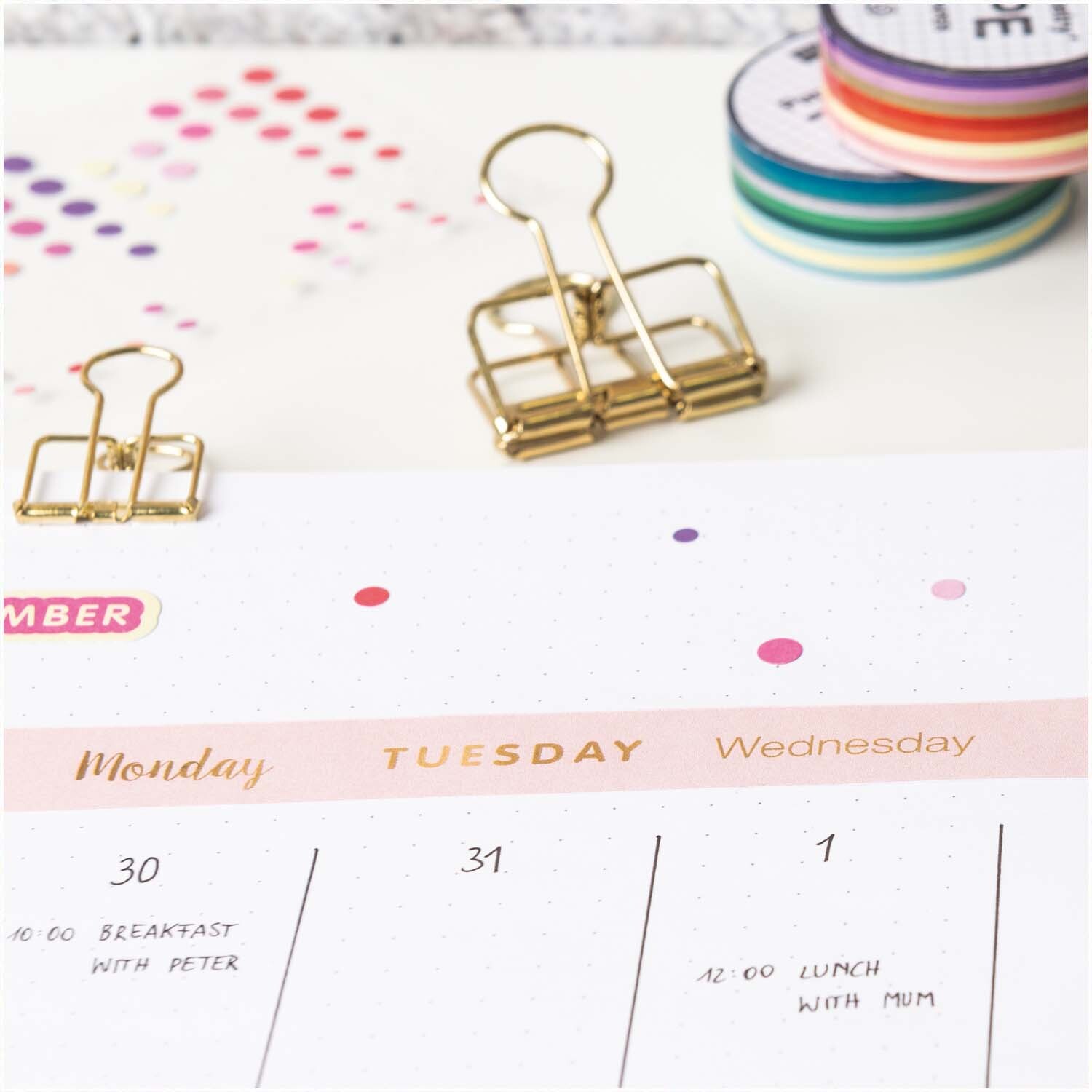 Paper Poetry Tape Wochentage in Rosa auf einem Kalender mit goldenen Klammern und bunten Washi-Tapes im Hintergrund.