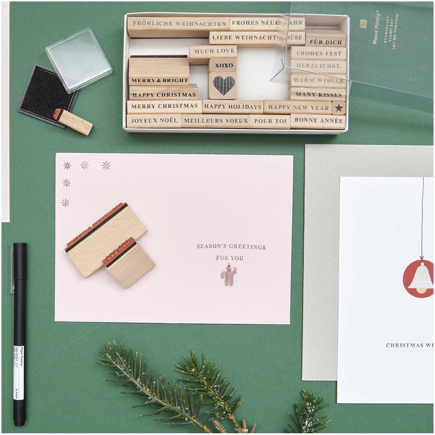 Paper Poetry XL Stempelset Merry Christmas Typewriter 27-teilig von Rico Design Paper Poetry XL Stempelset Merry Christmas Typewriter, 27-teilig, auf grünem Hintergrund mit Weihnachtskarten und Tannenzweig.