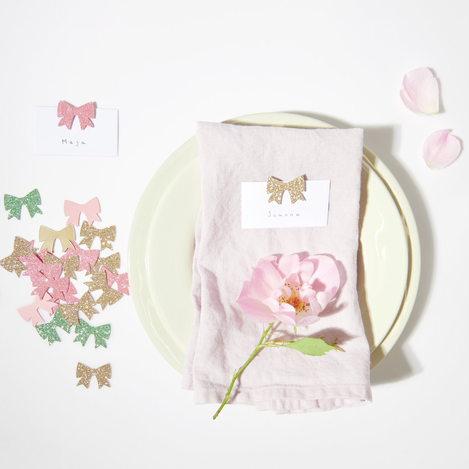 Streudekoration Schleifen Glitzer 20g 30x25mm Farbe Grün von Rico Design Streudekoration Schleifen Glitzer auf einem Tisch mit rosa Blume und Namenskarten, ideal für festliche Anlässe.