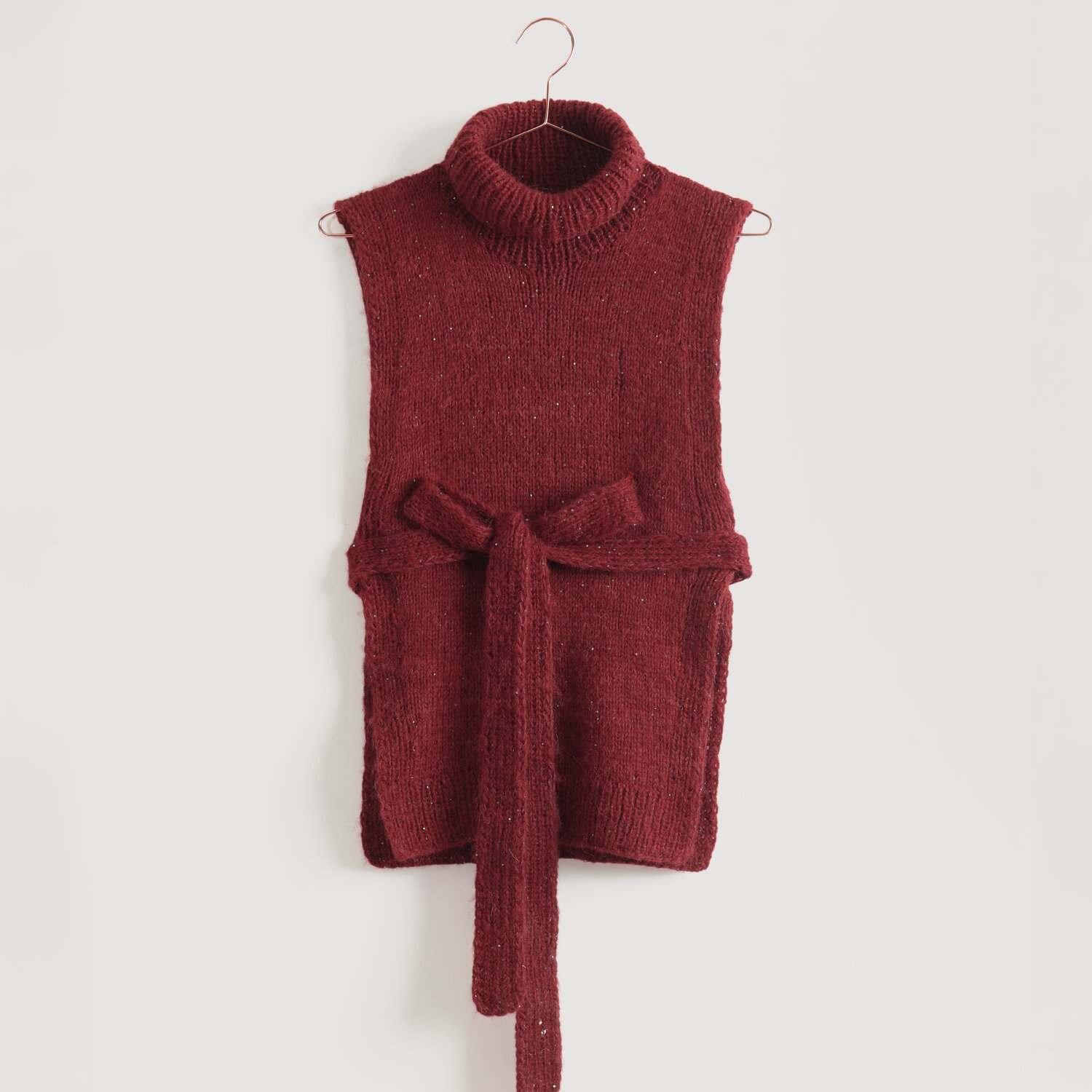 Luxury Merino Alpaca Dream aran 50g 125m Farbe Bordeaux von Rico Design Ärmelloser, roter Strickpullover mit Rollkragen und Bindegürtel, aufgehängt an einem Kleiderbügel. Marke: Modell Legeware. Perfekt für stilvolle, gemütliche Outfits.