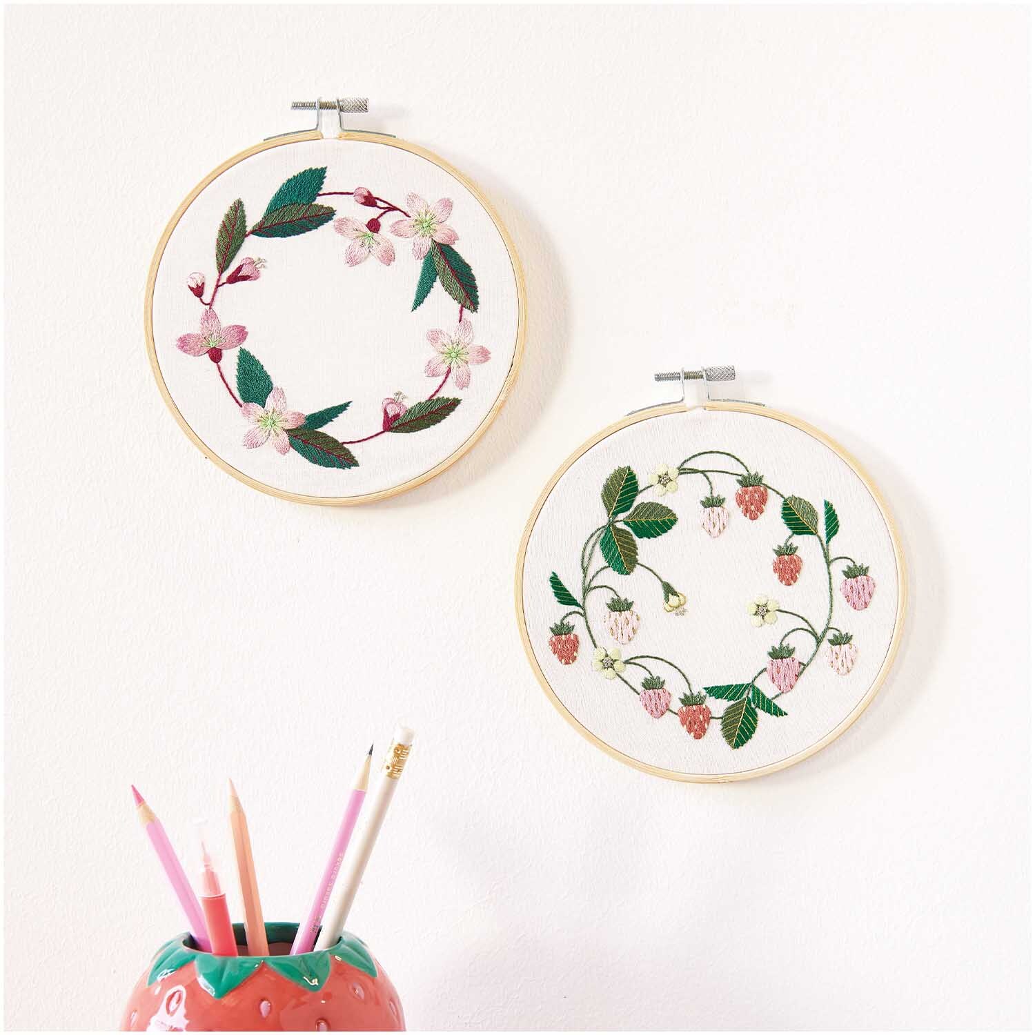 Kit de broderie couronne de fleurs de cerisier pré-dessiné from Rico Design Stickpackung Kirschblütenkranz vorgezeichnet: Zwei Stickrahmen mit floralen Motiven an einer weißen Wand, von Rico Design.