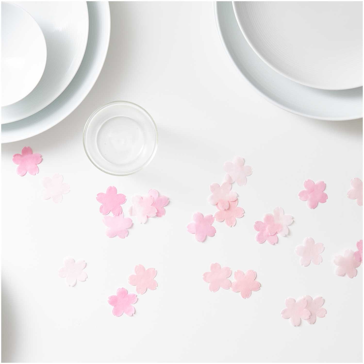 Konfetti Kirschblüten pastell rosa Mix 20g von Rico Design auf einem weißen Tisch mit Geschirr.