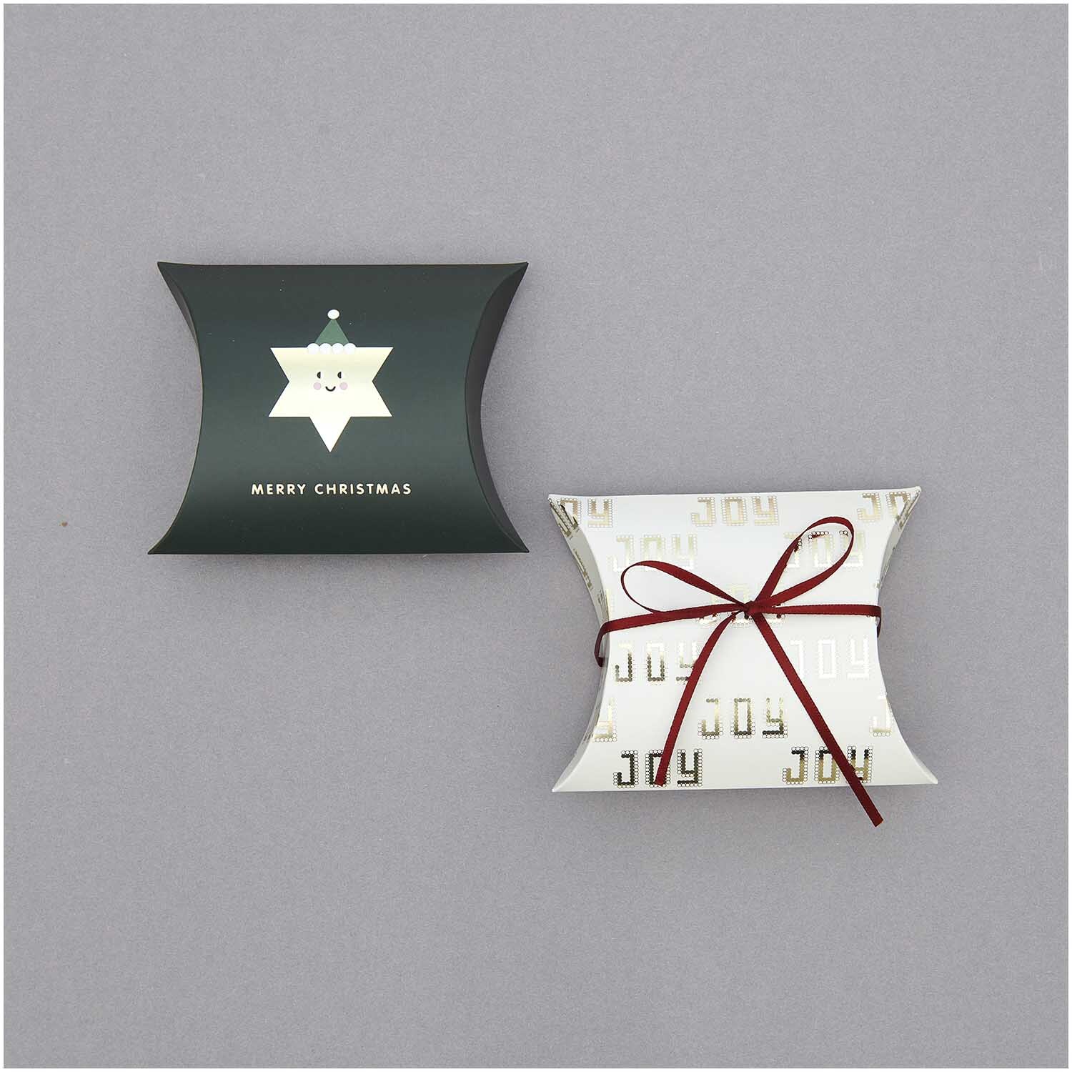 Paper Poetry Satinband 3mm 3m in Bordeaux ziert zwei Geschenkboxen, eine in Dunkelgrün mit Sternmotiv und eine in Weiß mit goldenen Buchstaben.