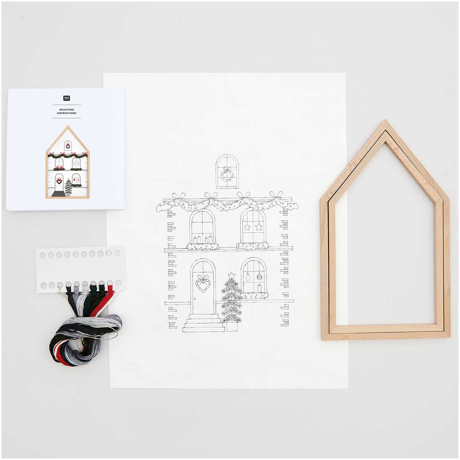 Paquet de broderie Maison grande dessinée 16x27cm from Rico Design Stickpackung Haus groß vorgezeichnet 16x27cm von Rico Design mit Holzrahmen, Garn und Anleitung auf weißem Hintergrund.