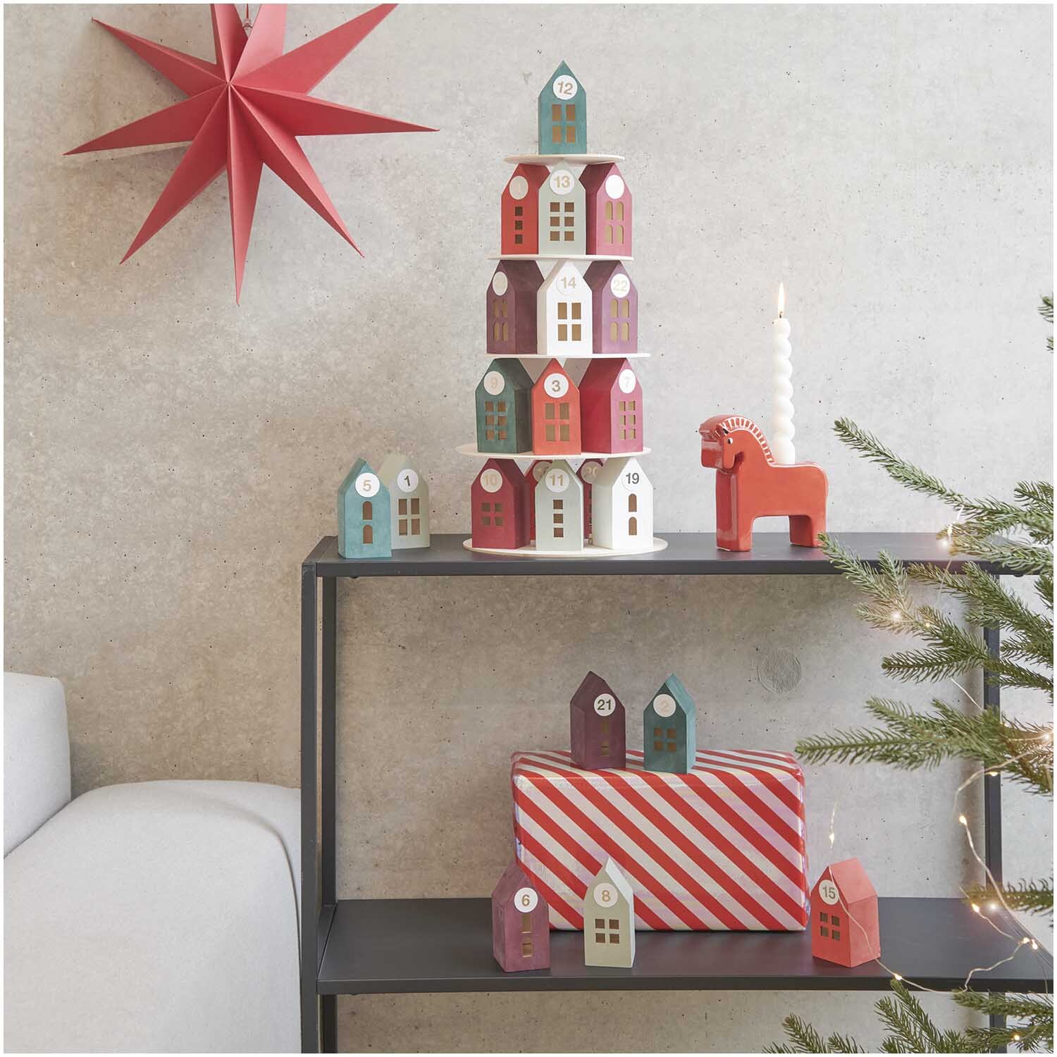 Adventskalender Holz-Haus-Pyramide von Rico Design Adventskalender Holz-Haus-Pyramide von Rico Design auf Regal mit rotem Stern und Geschenk.