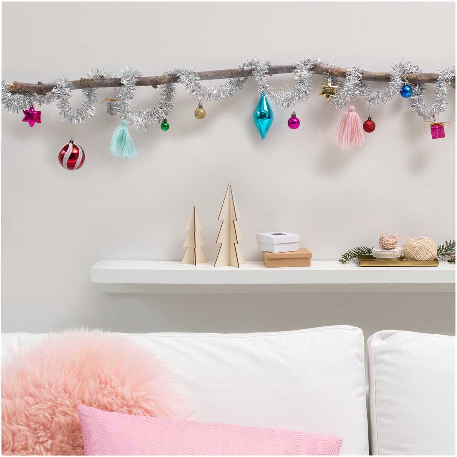 Girlande Lametta mit Dekor 2,5m von Rico Design Girlande Lametta mit Dekor 2,5m, mehrfarbig, dekoriert mit bunten Kugeln und Anhängern an einem Ast über einem weißen Sofa.