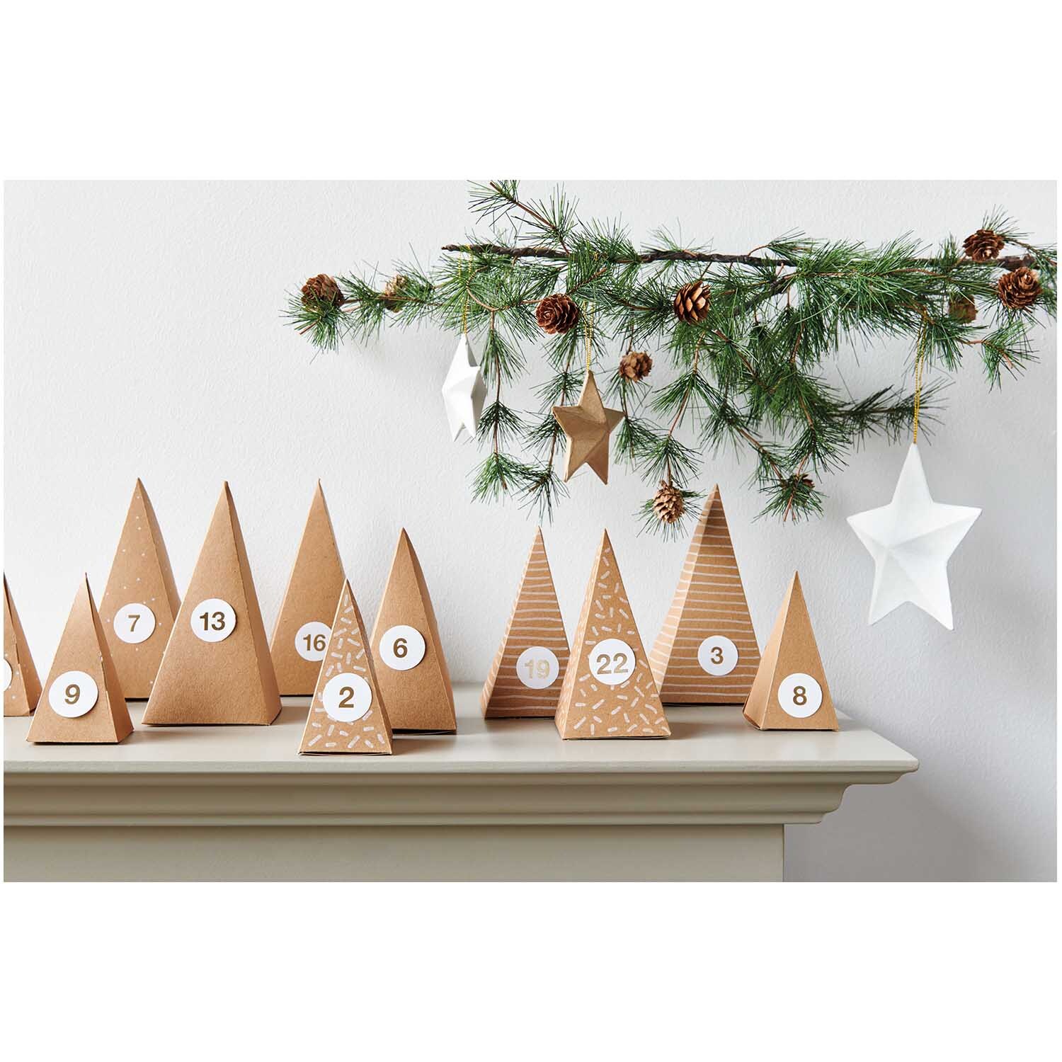 Paper Poetry Adventskalender Bäume 24 Stück Farbe Kraftpapier von Rico Design Paper Poetry Adventskalender Bäume 24 Stück aus Kraftpapier auf einem Regal, dekoriert mit Tannenzweigen und Sternen.