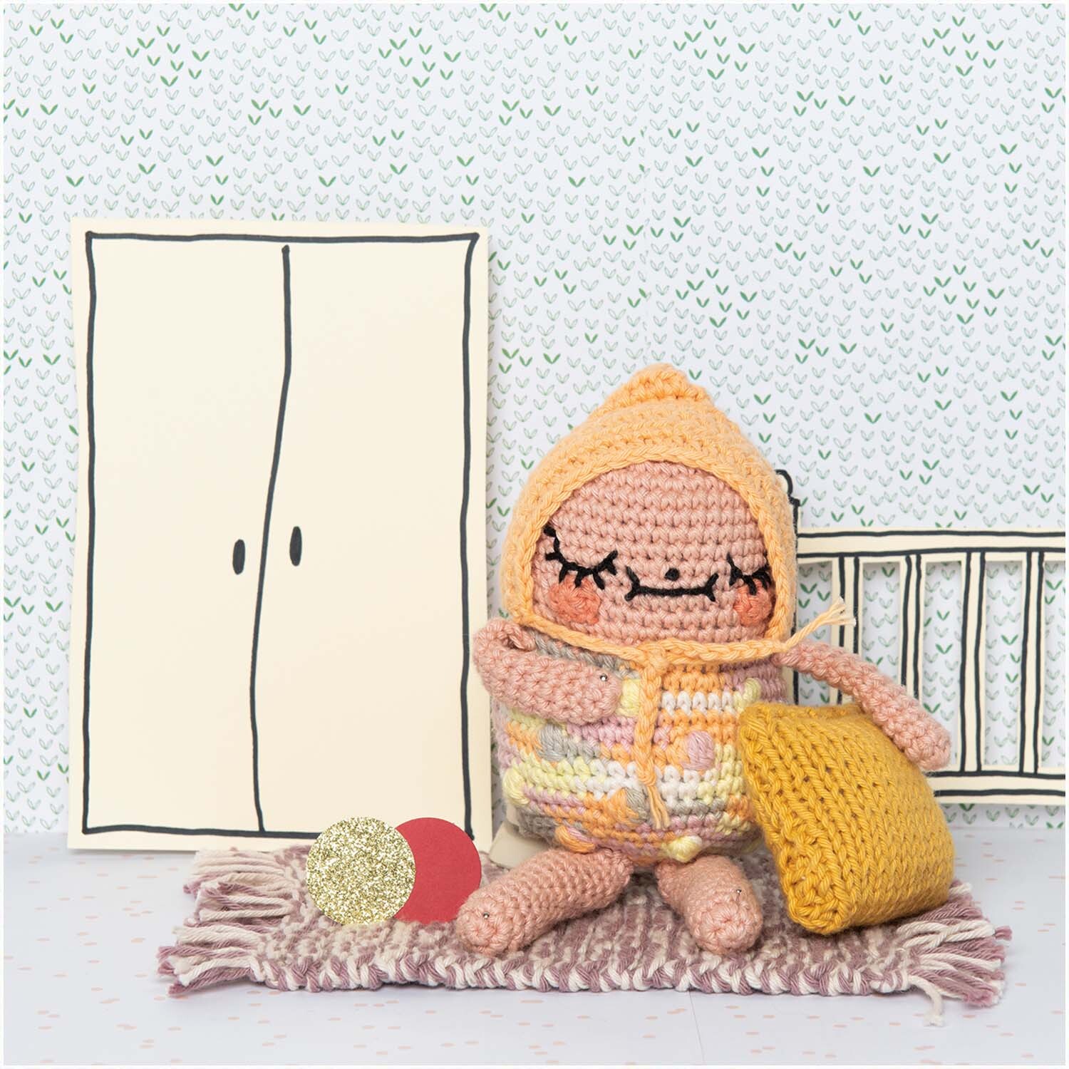 Ricorumi Crazy Cute Family deutsch von Rico Design Ricorumi Crazy Cute Family deutsch: Häkelfigur in buntem Outfit sitzt auf Teppich mit gelbem Kissen, vor gezeichneter Wand.