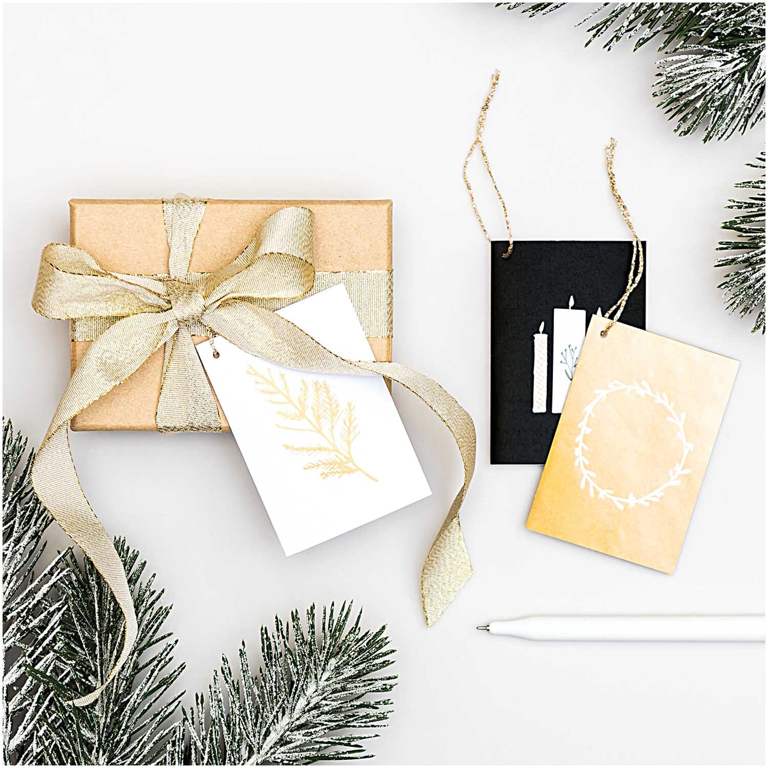 Paper Poetry Kärtchenanhänger Nostalgic Christmas: Drei elegante Anhänger in Schwarz-Gold und Weiß, dekoriert mit weihnachtlichen Motiven, neben einem Geschenk.
