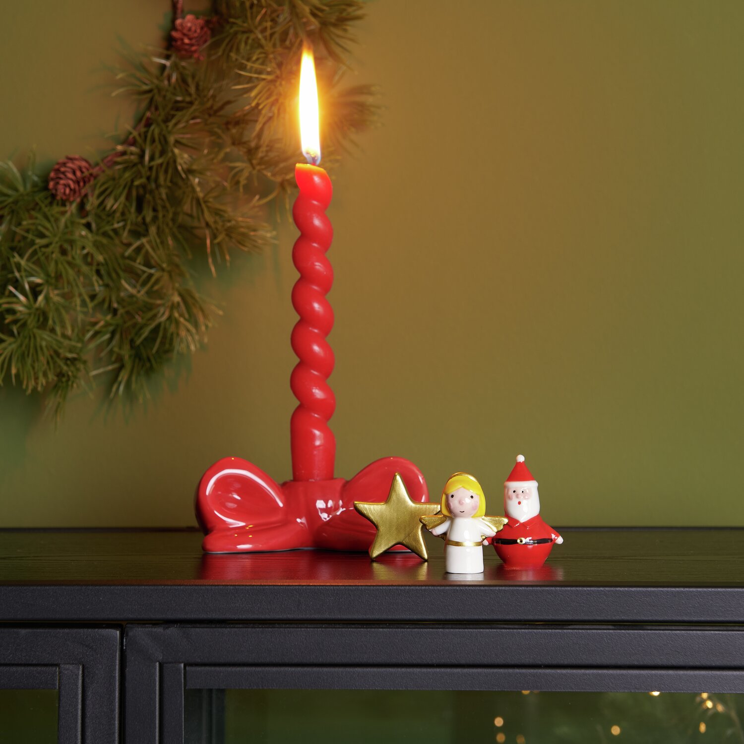 Bougeoir en porcelaine avec nœud 5 x 12,3 x 6,3 cm Couleur Rouge from Rico Design Porzellan Kerzenhalter Schleife mit roter Kerze, Engel in Weiß/Gold und Santa in Rot auf schwarzem Schrank.