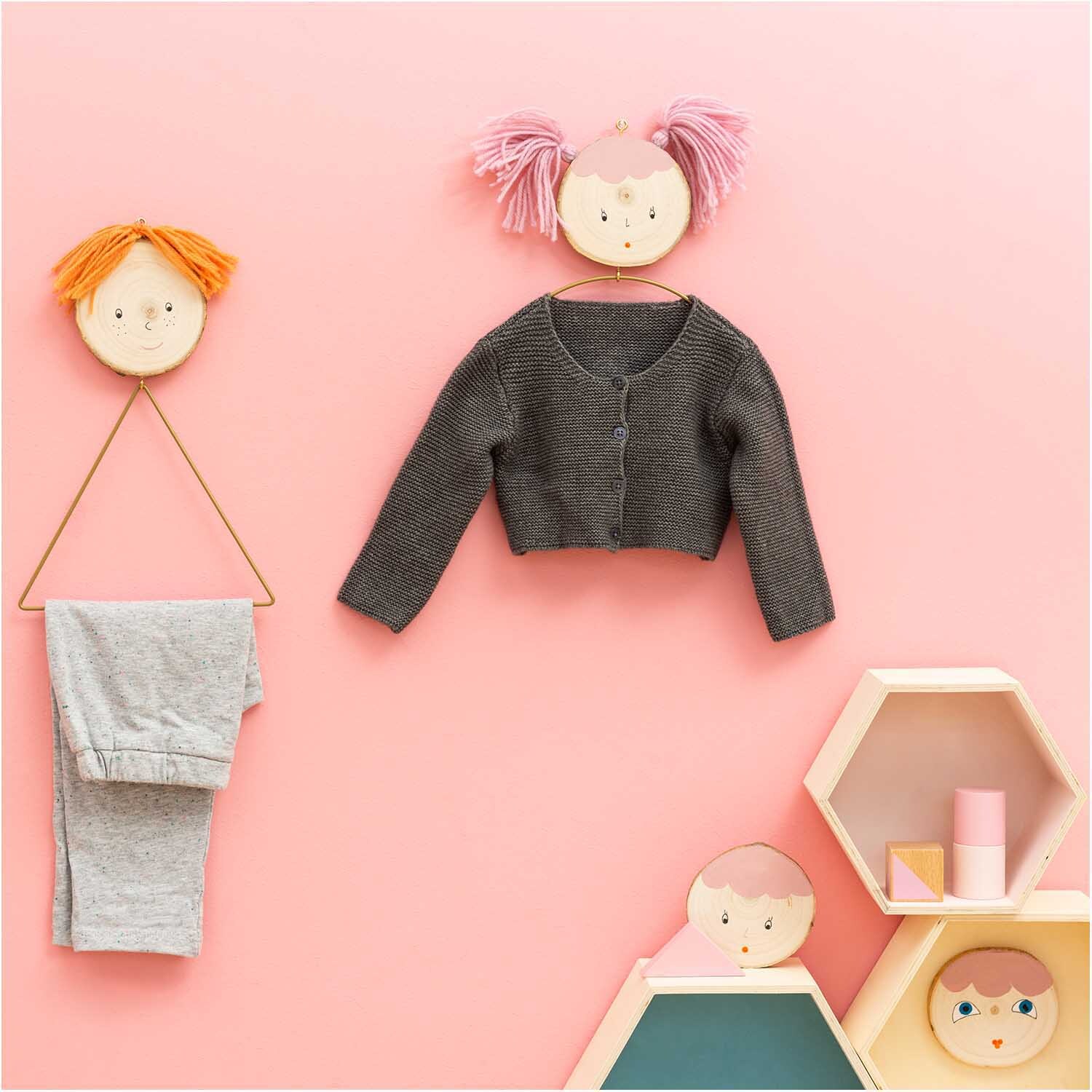 Holzbox Set sechseckig, dekorativ aufgestellt mit Kinderkleidung und Puppenköpfen an rosa Wand.