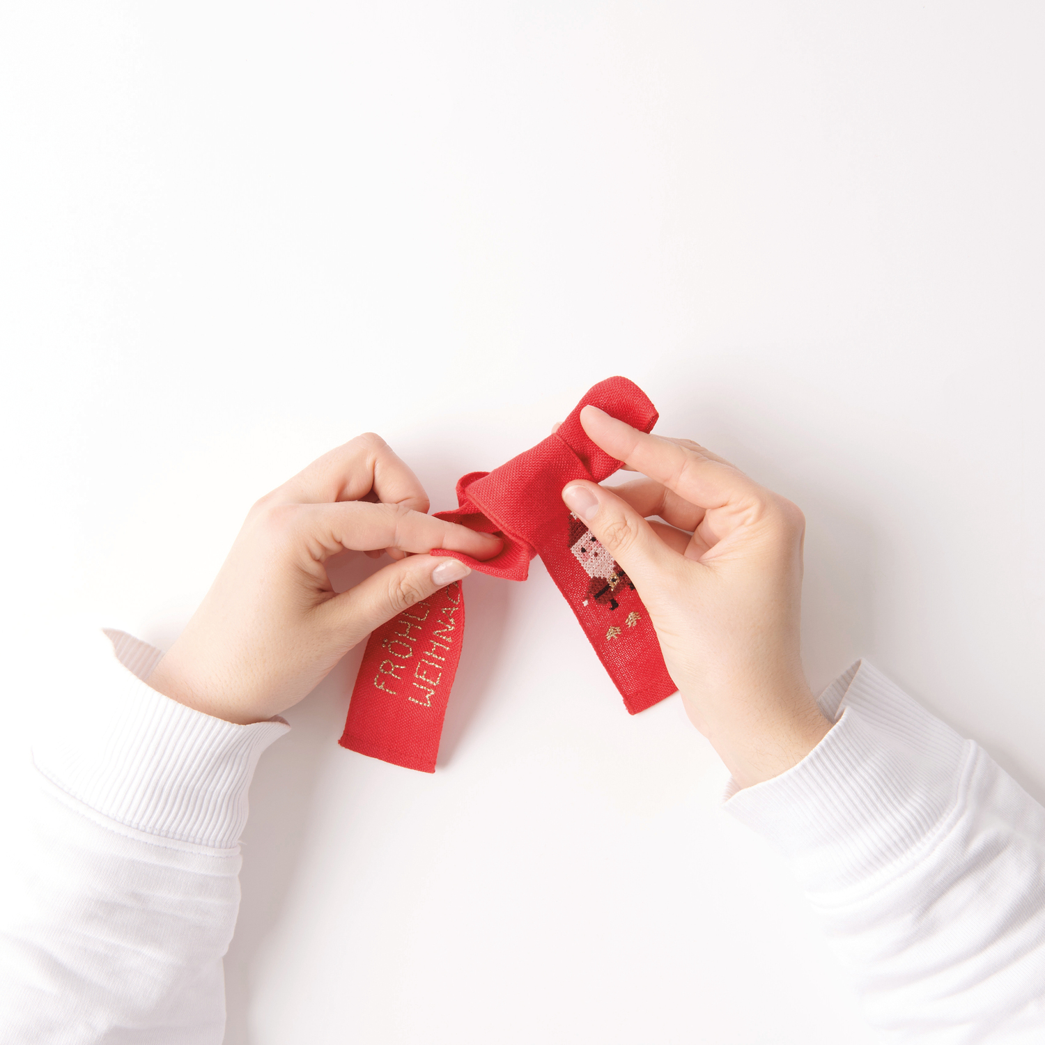 Stickpackung Schleife Nikolaus 12x19cm von Rico Design Stickbuch Put a Bow on It Nr. 185: Hände binden rote Schleife mit Nikolausmotiv, 12x19cm.