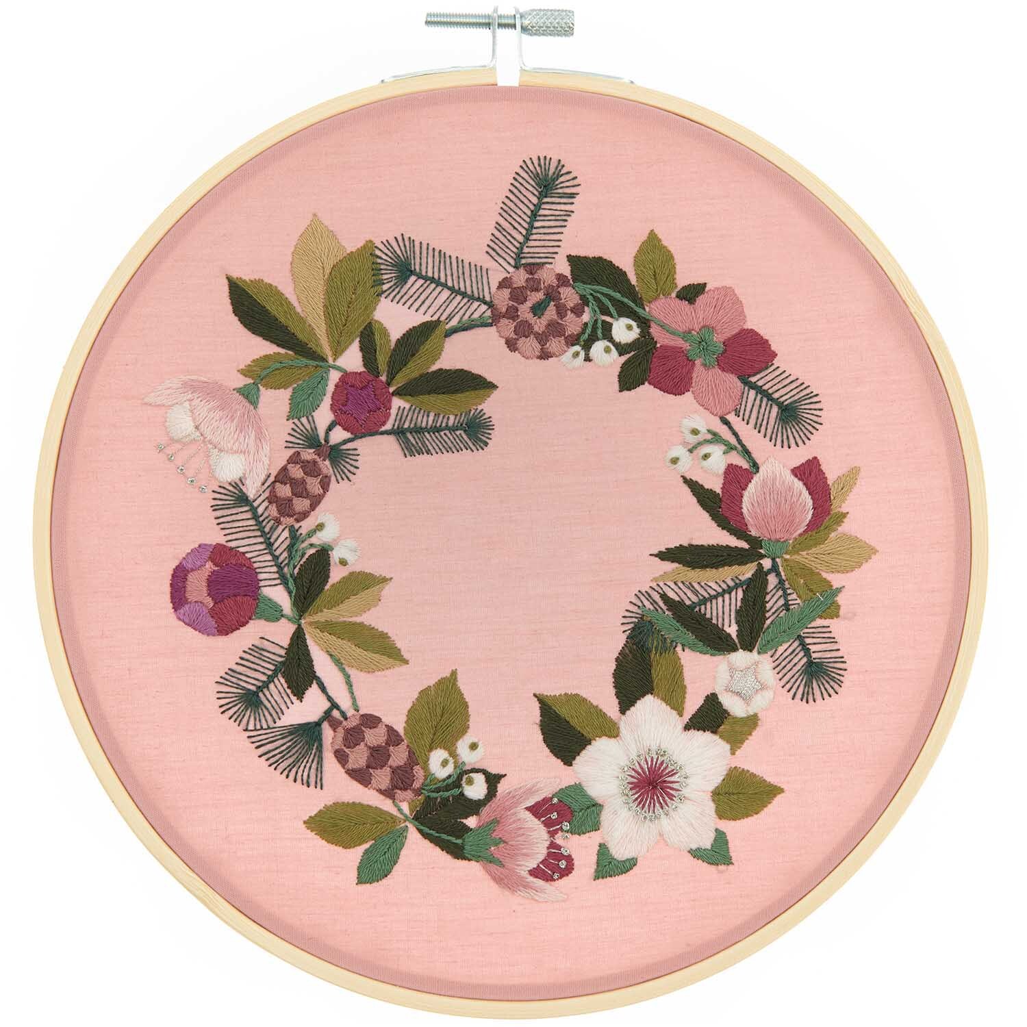 Stickpackung Bild Christrosen vorgezeichnet zeigt einen floralen Kranz auf rosa Stoff, Ø20,5cm, von Rico Design.