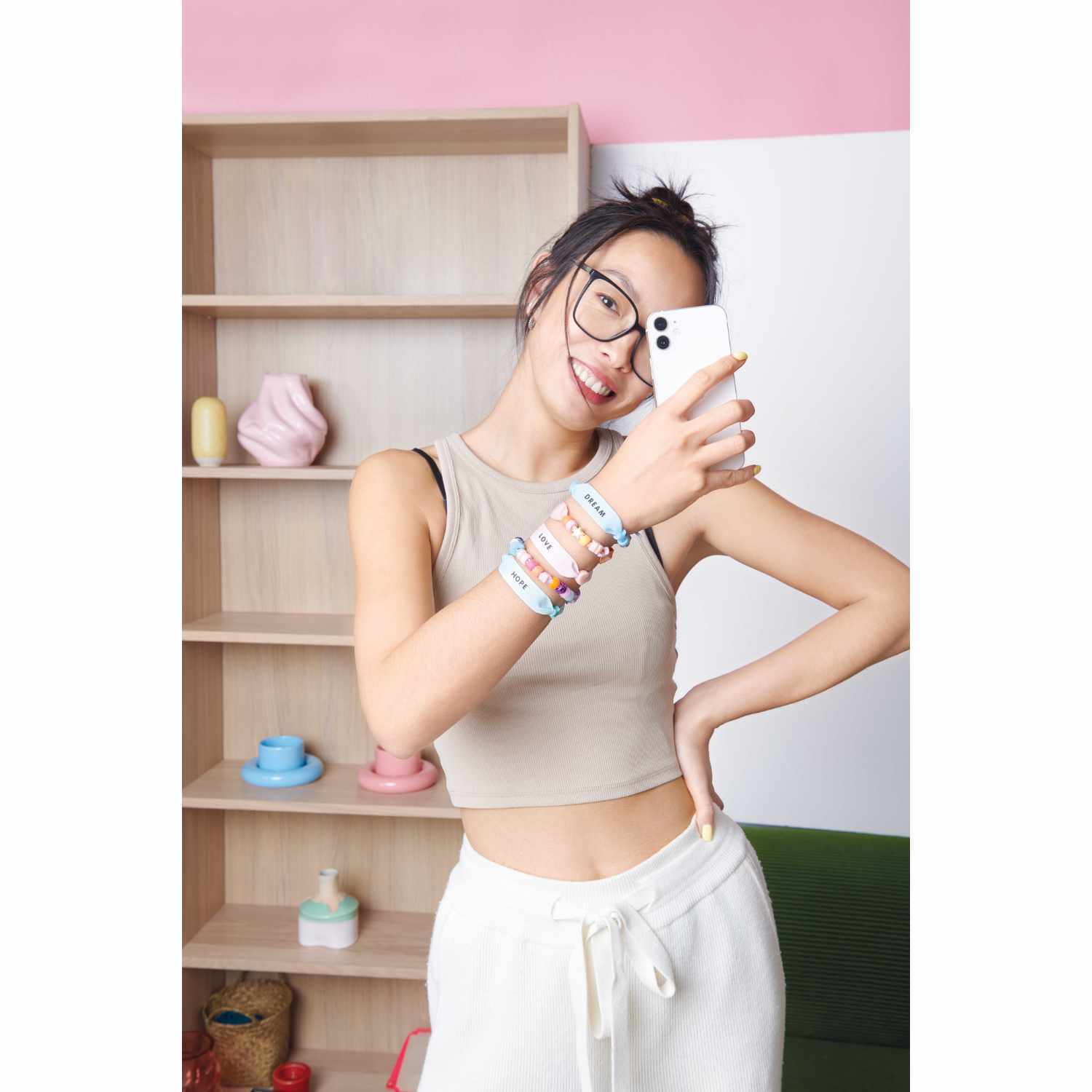 itoshii - Ponii Beads Bügelmotiv Schriftzüge 8 Designs von Rico Design itoshii - Ponii Beads Bügelmotiv Schriftzüge 8 Designs. Junge Frau mit Armbändern macht ein Selfie vor einem Regal mit Deko.