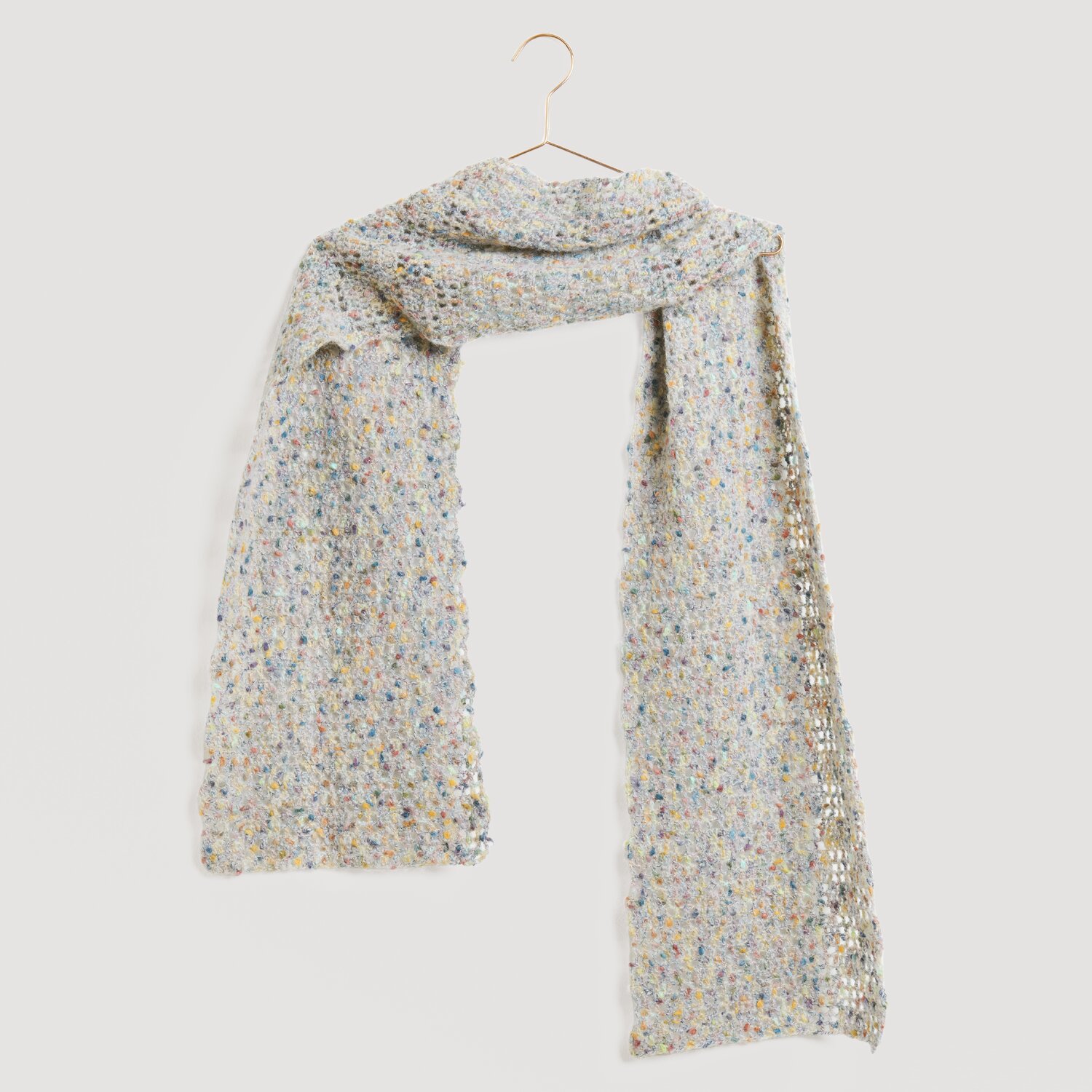 Fashion Cotton Alpaca Fun Neps 50g 215m Farbe Natur von Rico Design Ein eleganter, hellgrauer Schal mit bunten Akzenten, aufgehängt an einem goldenen Haken. Marke: Modell Legeware. Perfekt für stilvolle Outfits und vielseitige Kombinationen.