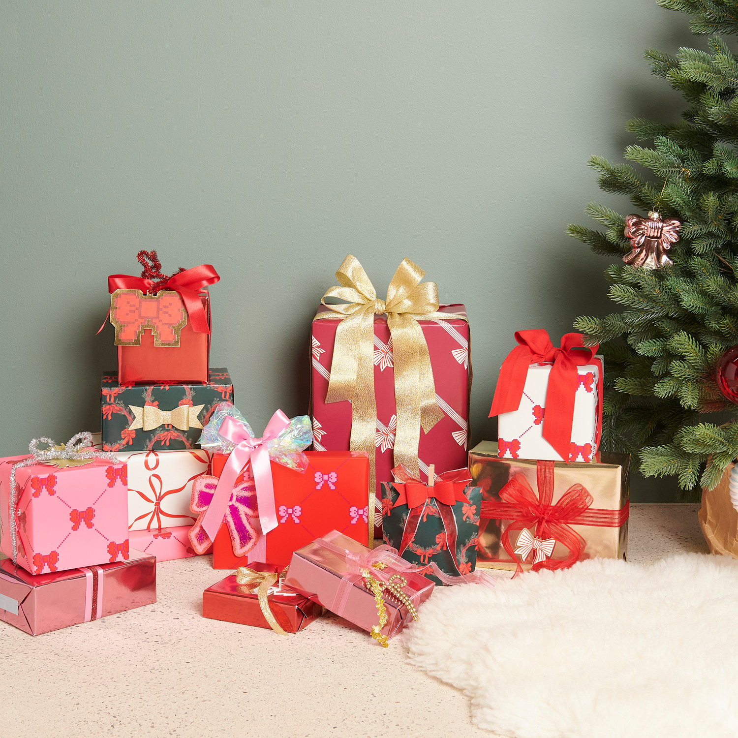 Satinband glänzend 25mmx3m von Rico Design Organzaband Grob Pink/Gold: Geschenke in Rot und Gold mit Schleifen, vor einem Weihnachtsbaum arrangiert.