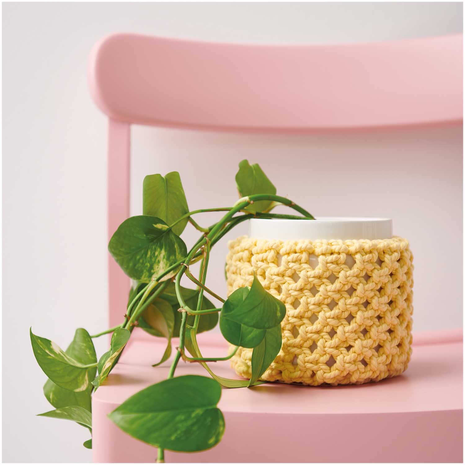 Creative Cotton Cord Makramee-Garn umhüllt einen Blumentopf auf einem rosa Stuhl, dekoriert mit grünen Blättern.