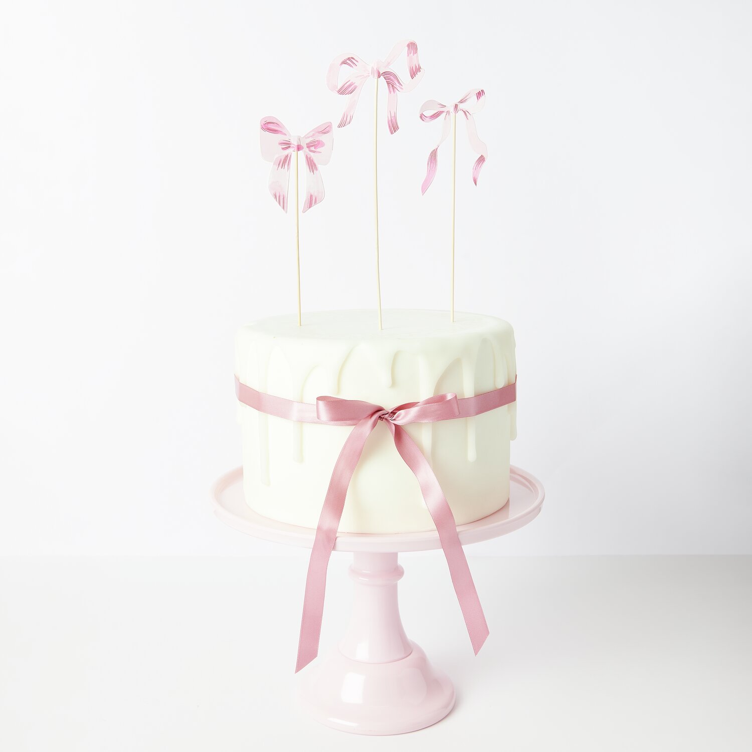 Picker Schleifen S Rosa 6 Stück von Rico Design Picker Schleifen S Rosa: Weiße Torte mit rosa Schleifen und Bändern von Rico Design, dekorativ auf rosa Tortenständer.