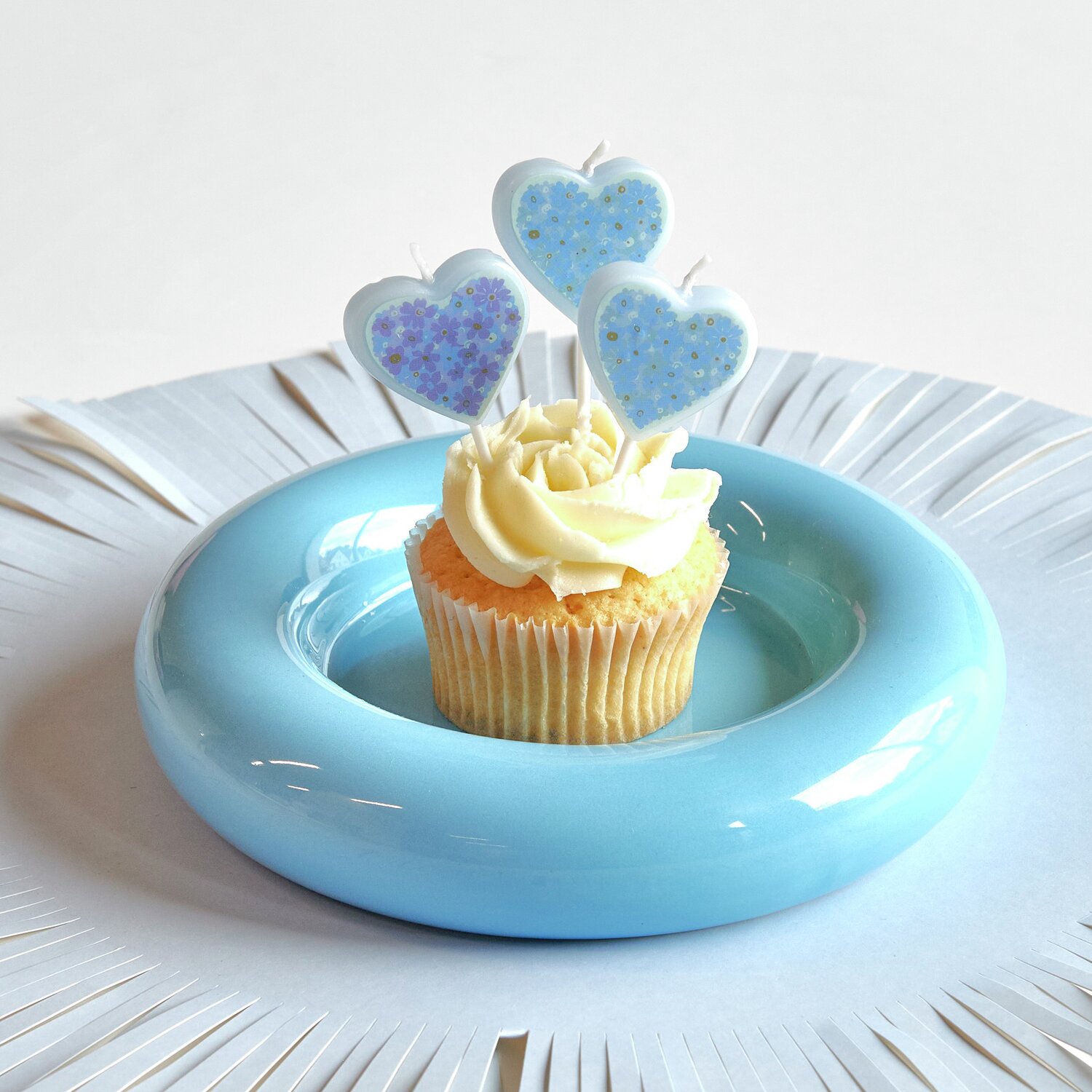 Kuchenkerzen Vergissmeinnicht 5 Stück von Rico Design Kuchenkerzen Vergissmeinnicht auf Cupcake mit blauer Glasur, dekoriert auf einem blauen Teller.