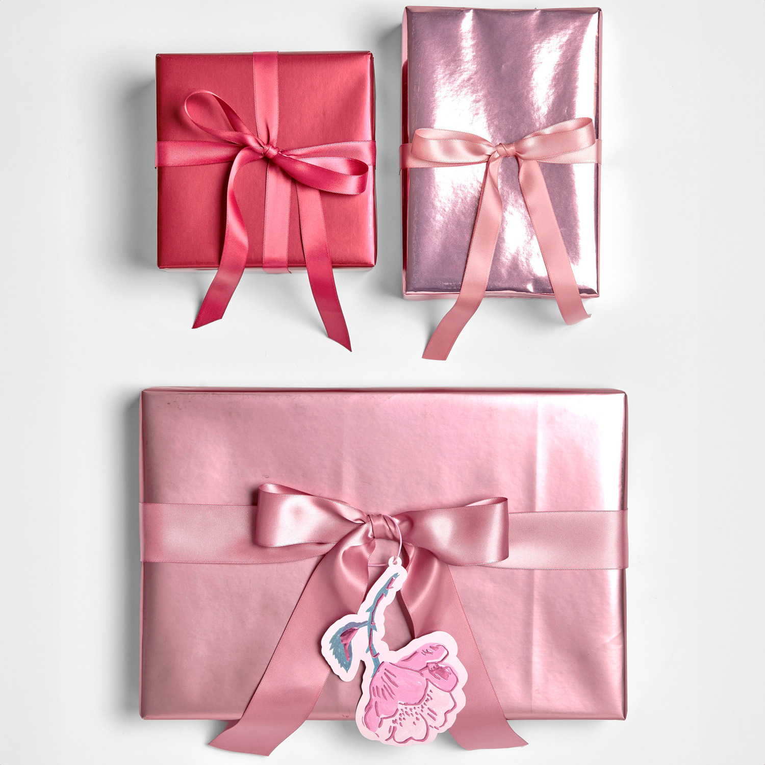 Geschenkpapier Metallic 70cm 2m 80g/m² Farbe Rosa von Rico Design Geschenkpapier Metallic Matt: Drei in Rosa und Rot verpackte Geschenke mit Schleifen, ideal für festliche Anlässe.
