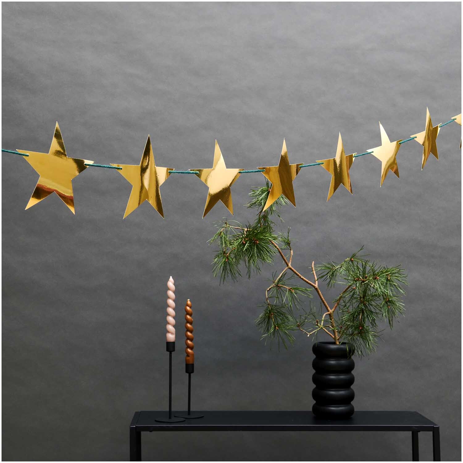 Paper Poetry Girlande Sterne gold 3m: Goldene Stern-Girlande dekoriert einen Tisch mit Kerzen und Zweigen.