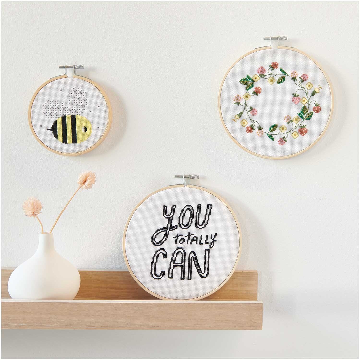 Stickpackung Erdbeerkranz Bild von Rico Design zeigt einen gestickten Kranz aus Erdbeeren und Blumen in einem Holzrahmen an der Wand.