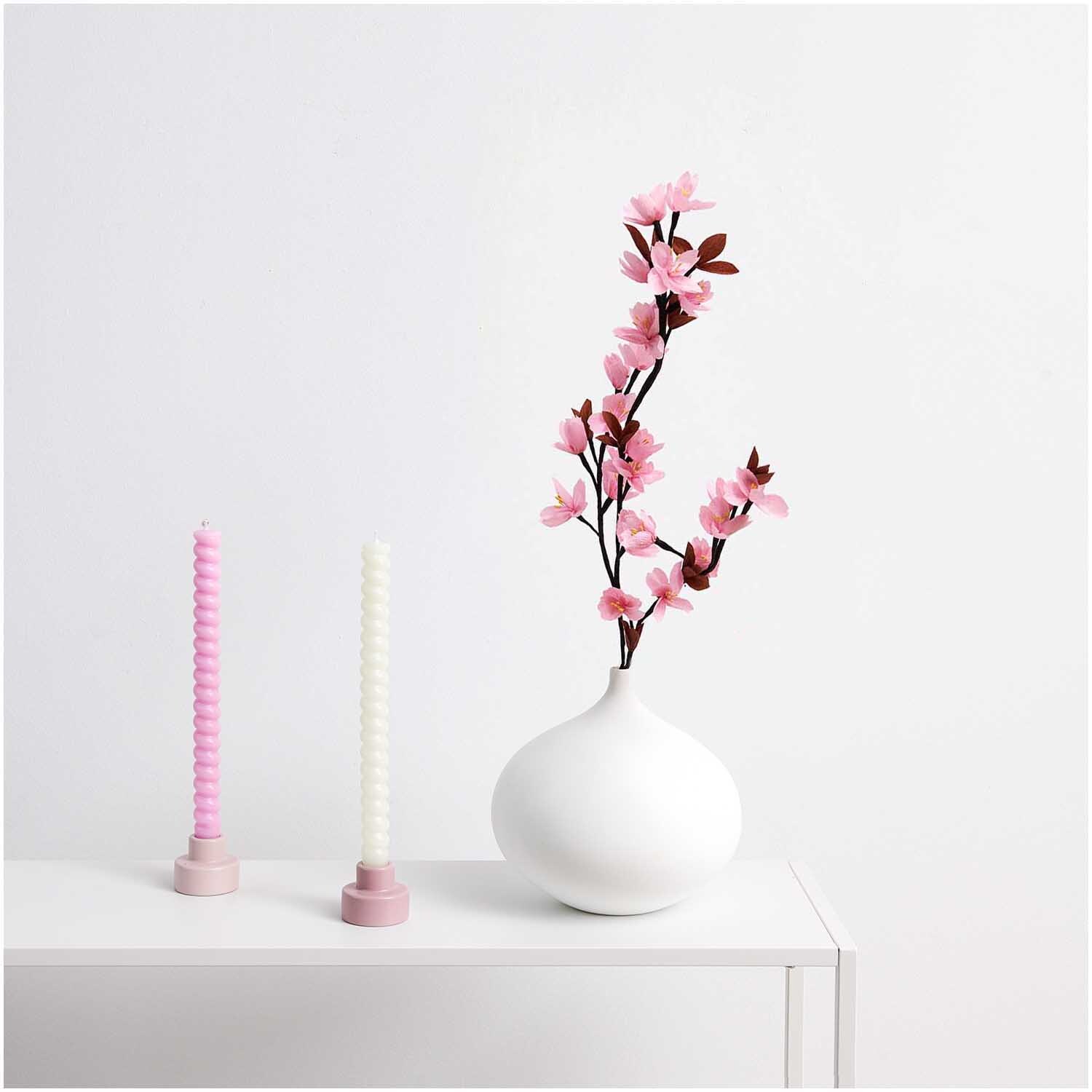 Spiralkerze 2,4x28cm neben einer weißen Vase mit Kirschblüten auf einem Tisch, von Rico Design.