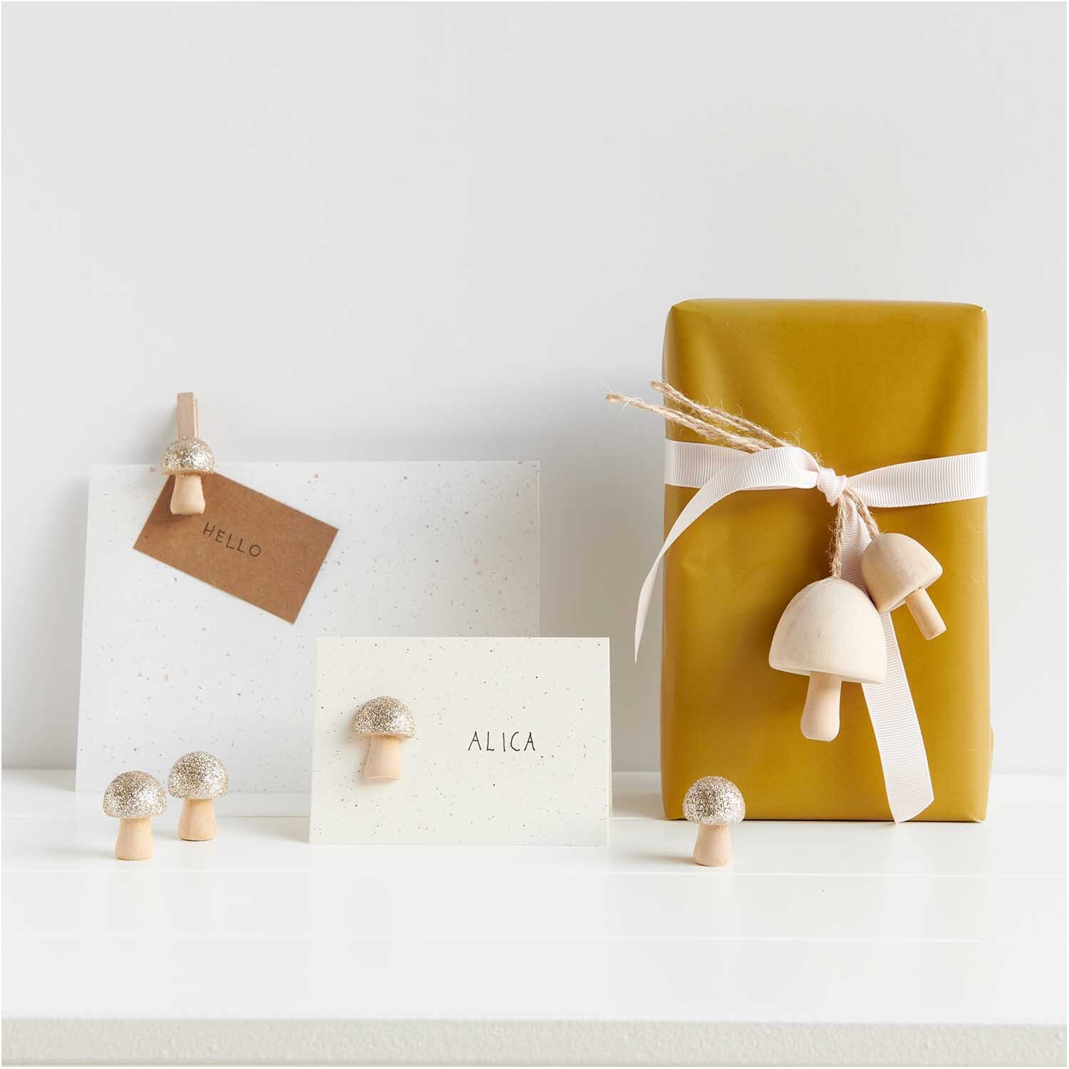 Holzanhänger Pilz klein natur 3x3,9cm von Rico Design Holzanhänger Pilz klein natur von Rico Design neben Geschenkverpackung und Karten auf weißem Hintergrund.