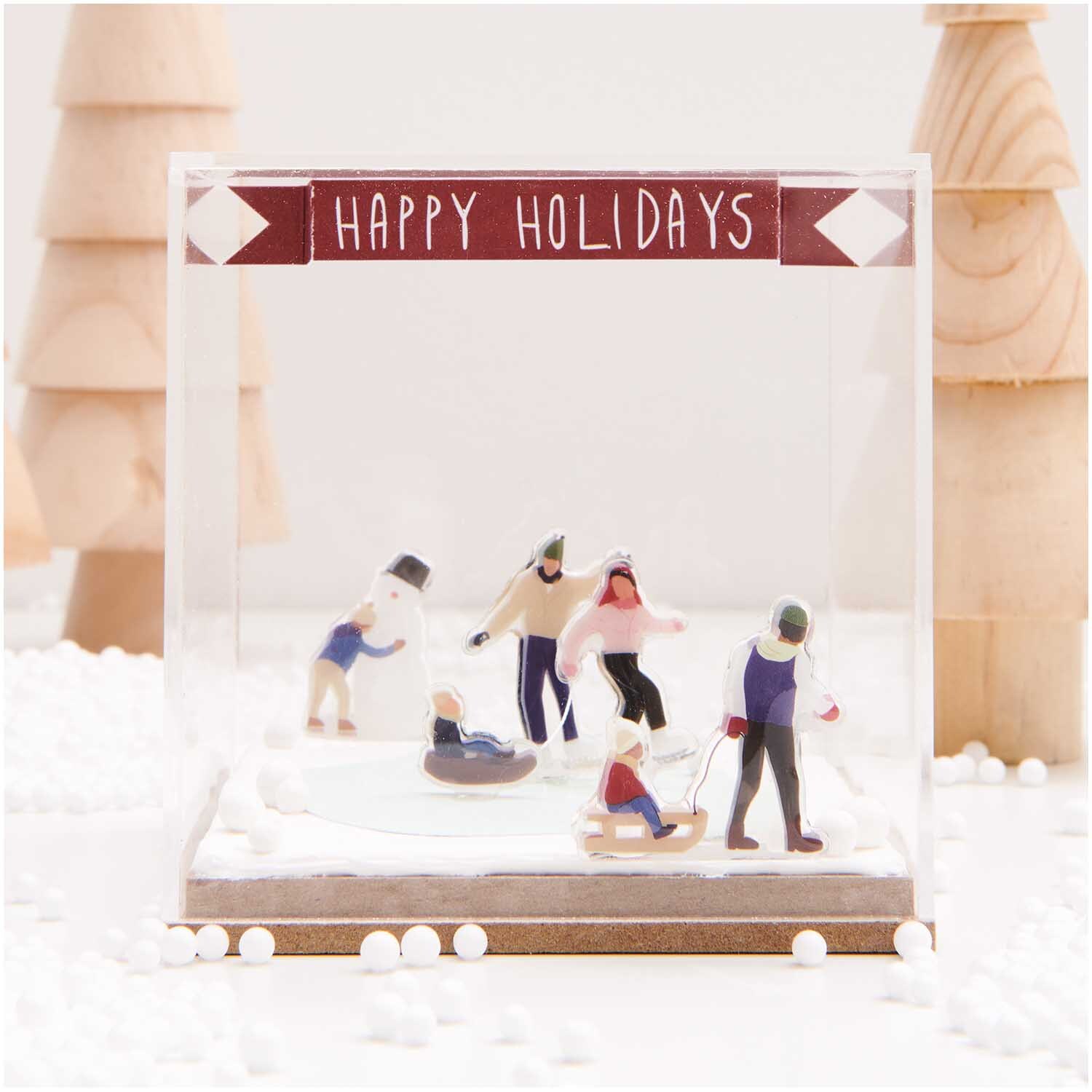 Figurico Modelliermasse 28g Farbe Weiß von Rico Design Figurico Modelliermasse 28g: Miniatur-Szene mit Menschen beim Wintersport in Schneelandschaft, dekoriert mit "Happy Holidays"-Banner.