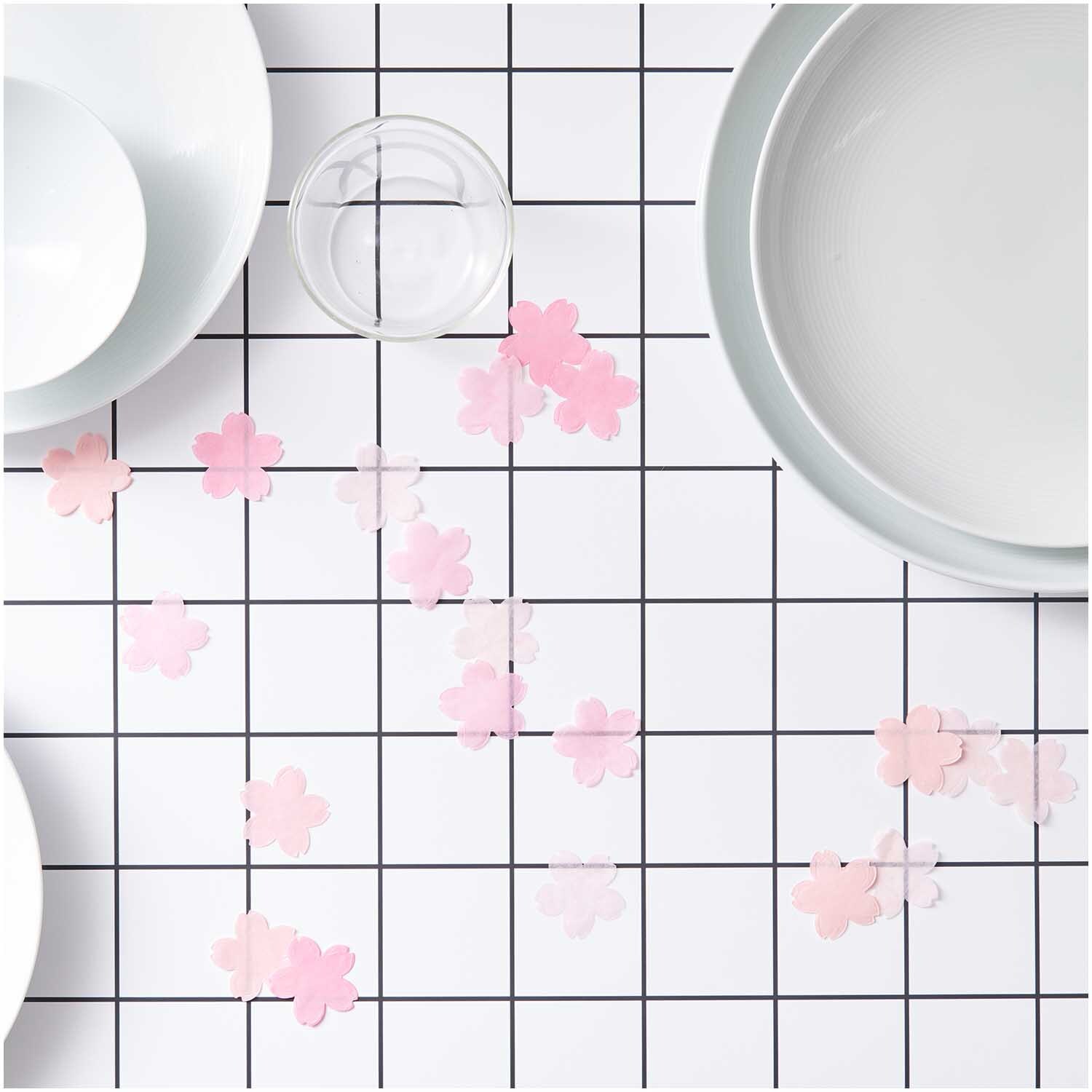 Konfetti Kirschblüten pastell rosa Mix 20g auf einem Tisch mit weißem Geschirr und Glas. Ideal für festliche Dekorationen.