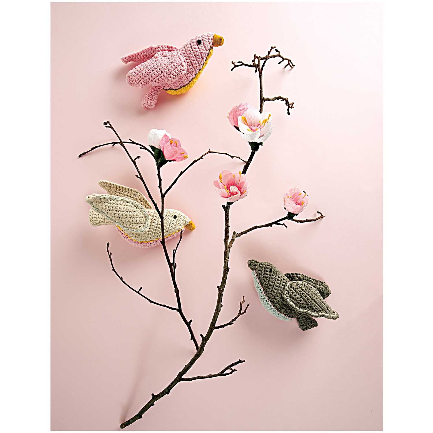 Füllwatte: Drei gehäkelte Vögel in Rosa, Beige und Grau sitzen auf einem blühenden Ast vor rosa Hintergrund.